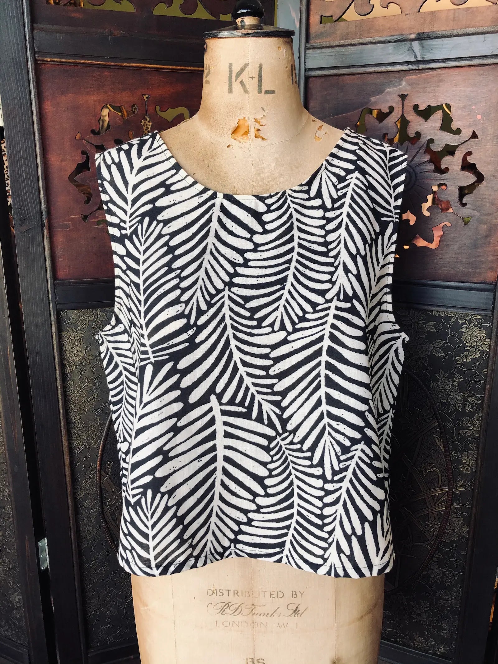 Broochella Moutaki  Black and white patterned leaf print top on a mannequin against a decorative wall.