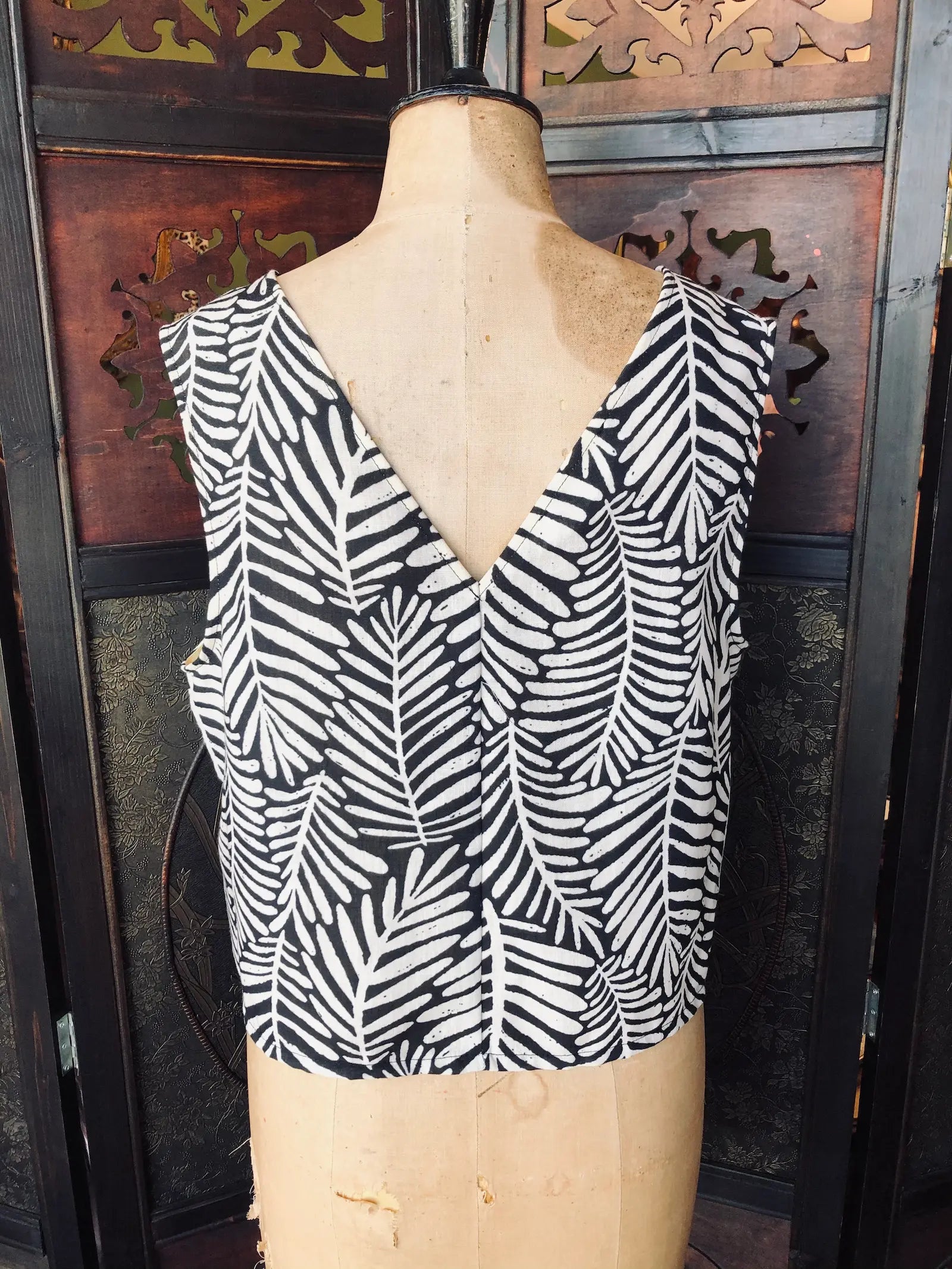 Broochella Moutaki Back view of  Black and white patterned leaf print top on a mannequin against a decorative wall.