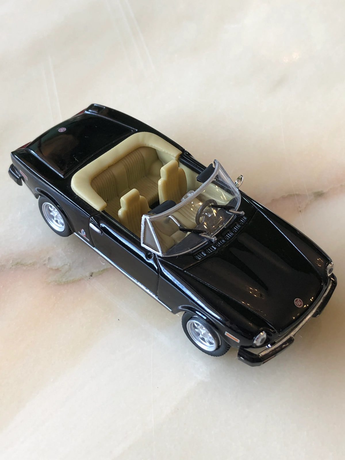 Broochella Nero Riviera No.84 Vintage Convertible Car Brooch in glossy black, featuring cream seats, a detailed dashboard, clear windscreen, silver wheels and chrome accents, photographed from an elevated three-quarter angle.