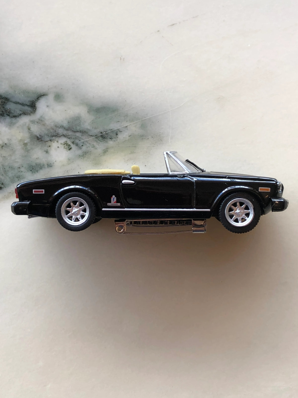 Broochella Nero Riviera No.84 Vintage Convertible Car Brooch in side profile, featuring a classic black roadster silhouette, cream interior, silver wheels, chrome detailing and metal brooch pin fastening underneath.