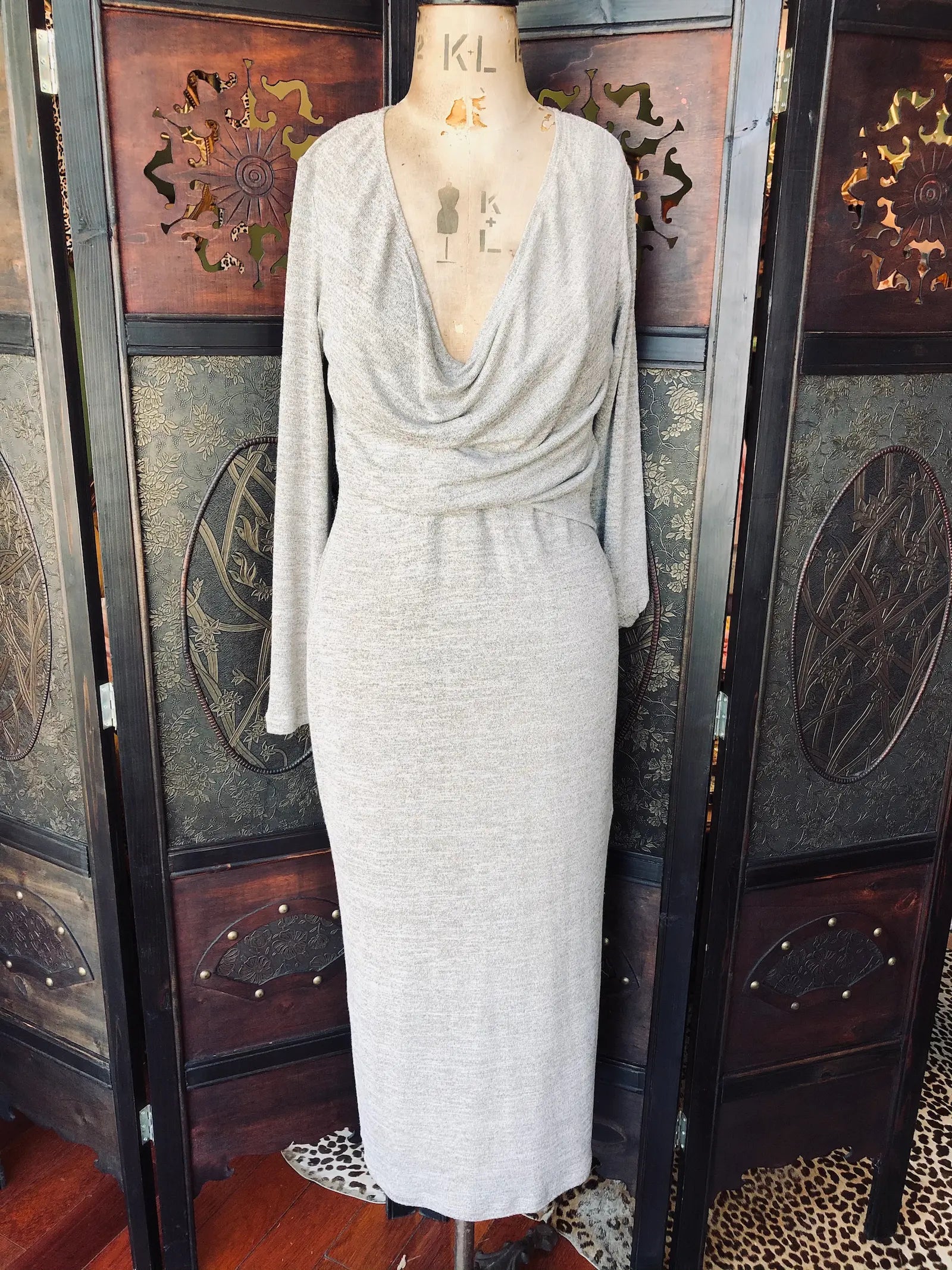  Broochella One Fell Swoop midi dress. Size: 12, grey, 90% Polyester, 10% Spandex With draped neckline and long sleeves. It is pictured on a vintage mannequin. The background is an ornate, vintage, dark wood room divider. 