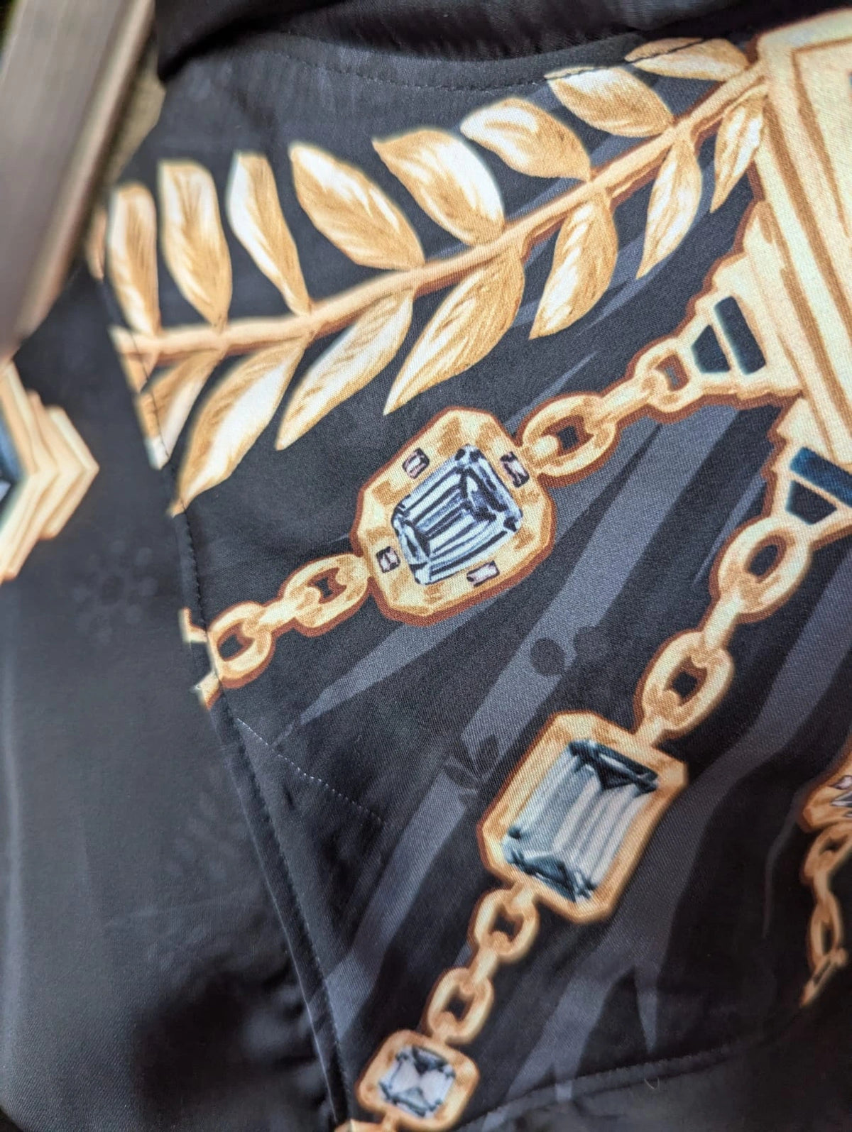 Broochella Paco Rabanne maxi dress.  Close-up of a flaw in fabric. The fabris is black and the print is gold chain with blue gemstones. 