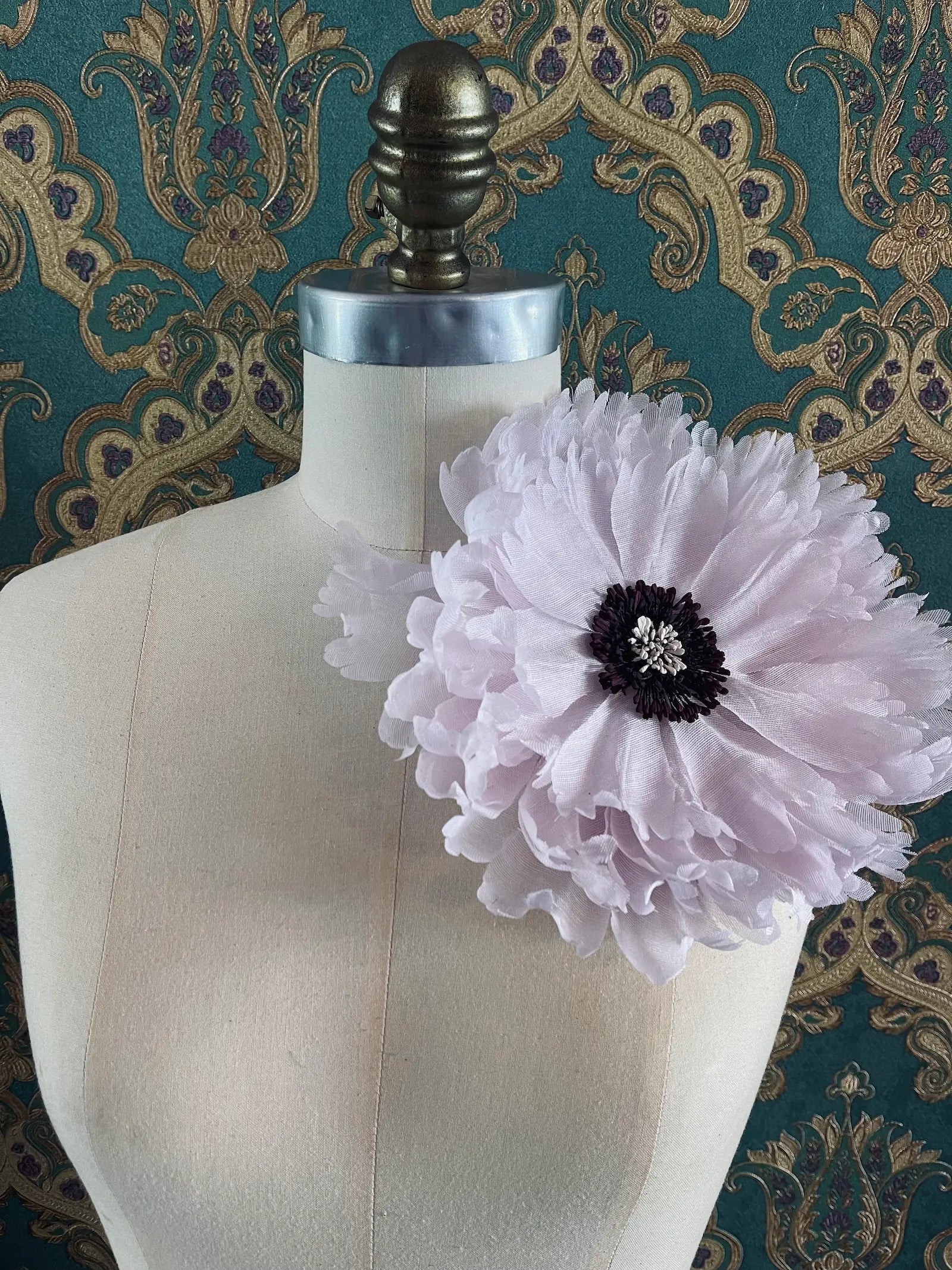 Broochella peone handmade large pink fabric flower brooch. Styled on a mannequin. The background is green and gold damask wallpaper