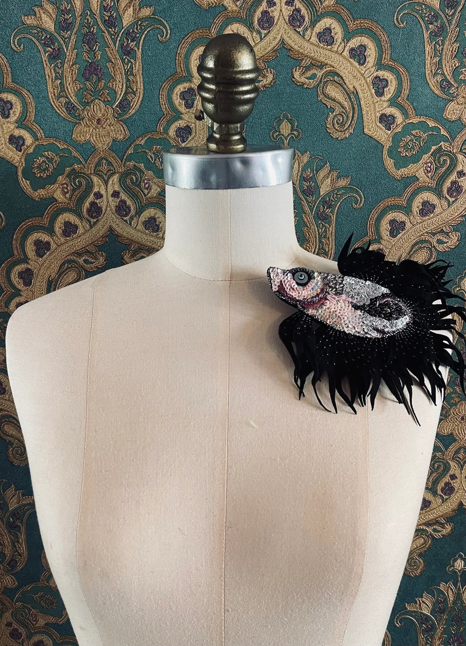 Broochella Pesce siamese fish hand beaded pink and black figural brooch Styled on a mannequin. The background is green and gold damask wallpaper