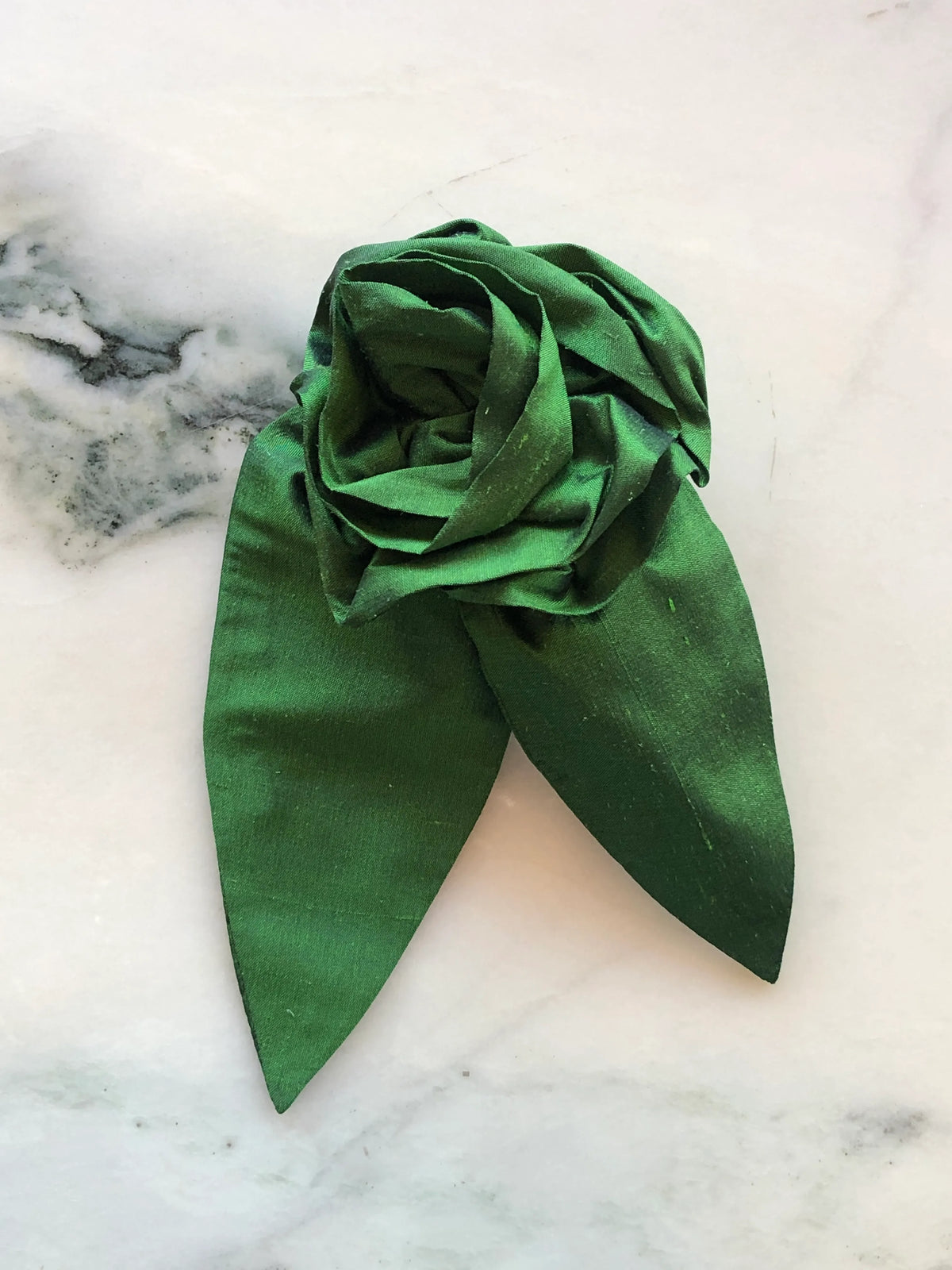 Broochella Petalo Large green silk flower brooch with sculptural rose petals and two pointed silk leaves, photographed on white marble with grey-green veining.
