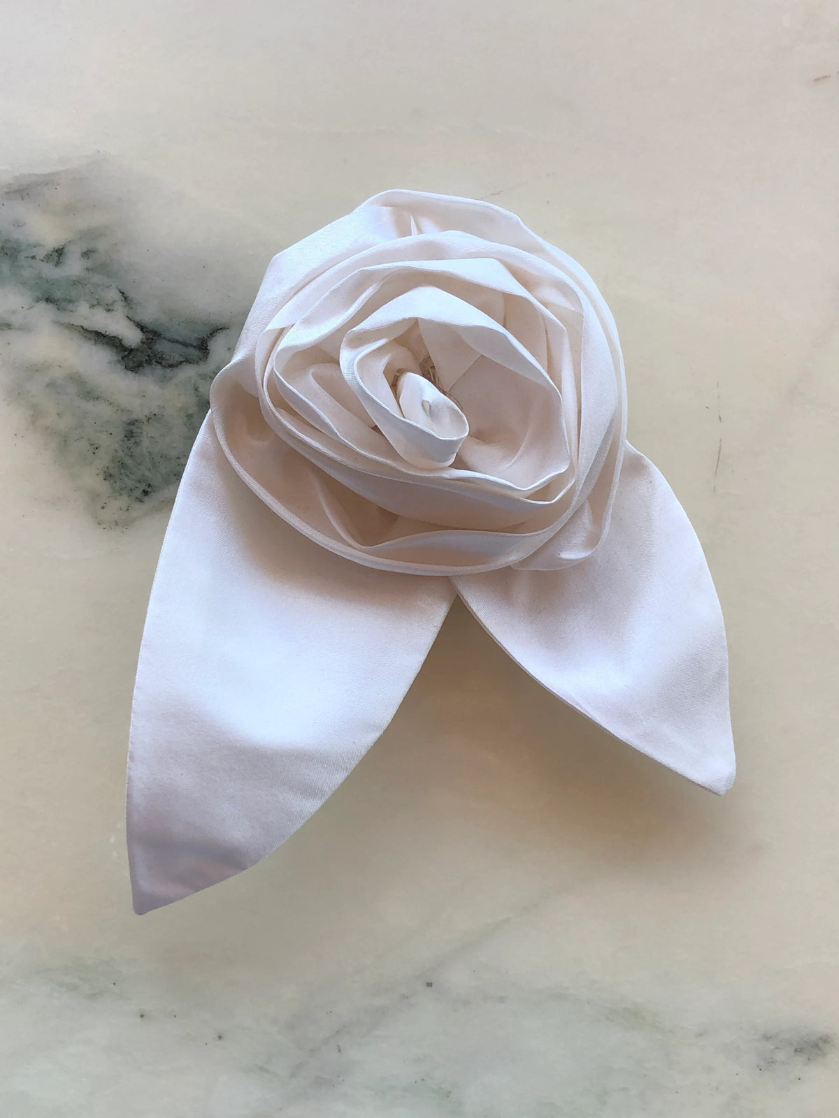 Broochella Petalo Large ivory silk flower brooch with sculptural rose petals and two pointed silk leaves, photographed on white marble with grey-green veining.