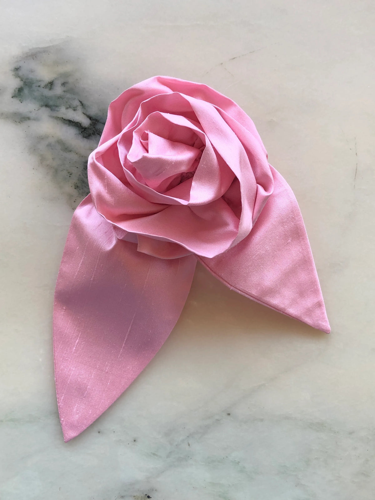 Broochella Petalo Large pink silk flower brooch with sculptural rose petals and two pointed silk leaves, photographed on white marble with grey-green veining.