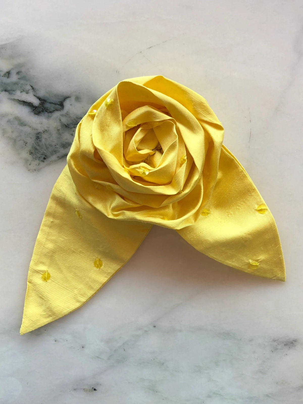 Broochella Petalo Large yellow silk flower brooch with sculptural rose petals, two pointed silk leaves and subtle embroidered details, photographed on white marble with grey-green veining.