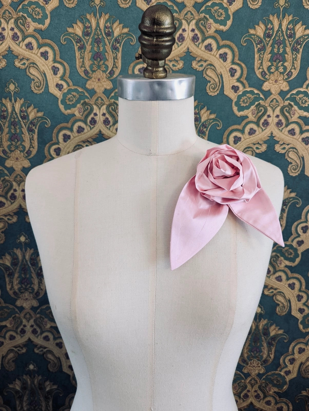 Broochella Petalo handmade silk flower brooch with petal detail in pink. Pinned to a mannequin. The background is green and gold damask wallpaper.