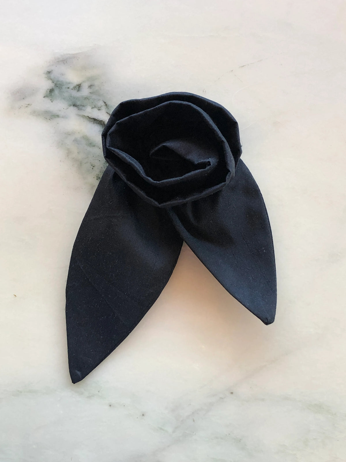 Broochella Petalo Men black silk flower brooch for men with sculptural rose petals and two pointed silk leaves, photographed on white marble with grey-green veining.
