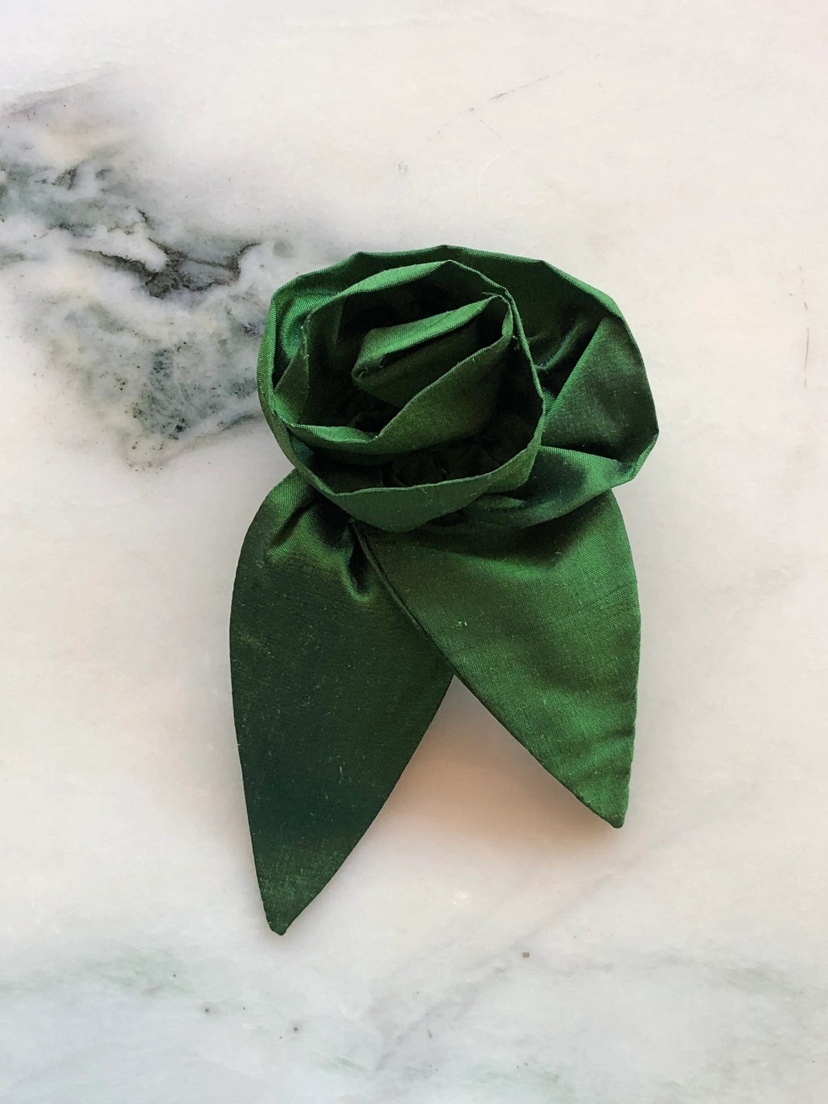 Broochella Petalo Men green silk flower brooch for men with sculptural rose petals and two pointed silk leaves, photographed on white marble with grey-green veining.