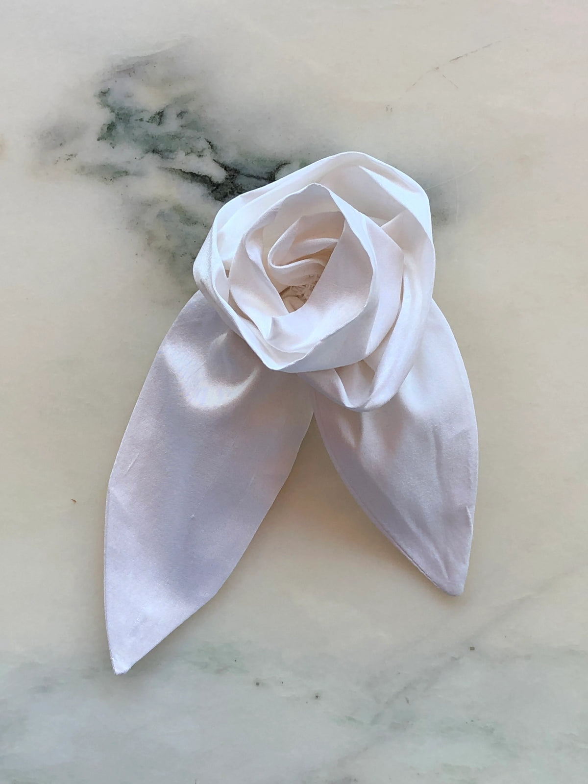 Broochella Petalo Small ivory silk flower brooch with sculptural rose petals and two pointed silk leaves, photographed on white marble with grey-green veining.