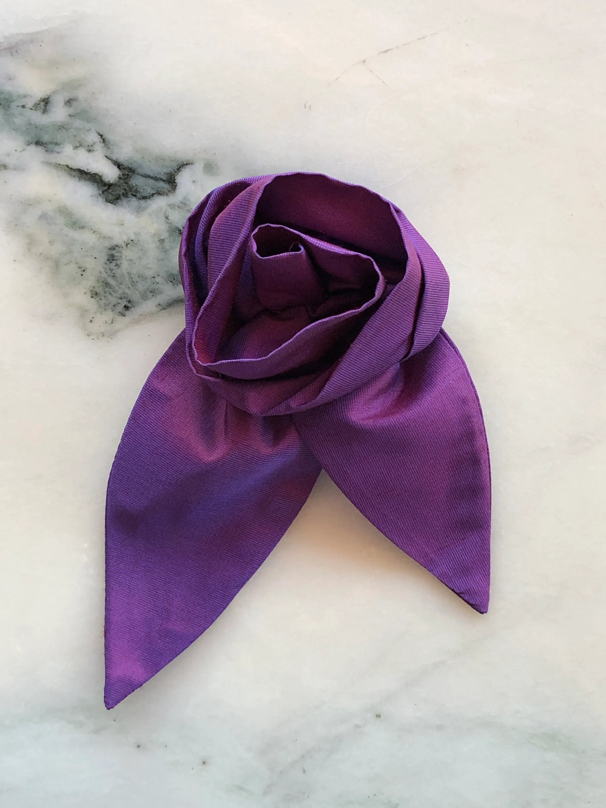 Broochella Petalo Men purple silk flower brooch for men with sculptural rose petals and two pointed silk leaves, photographed on white marble with grey-green veining.