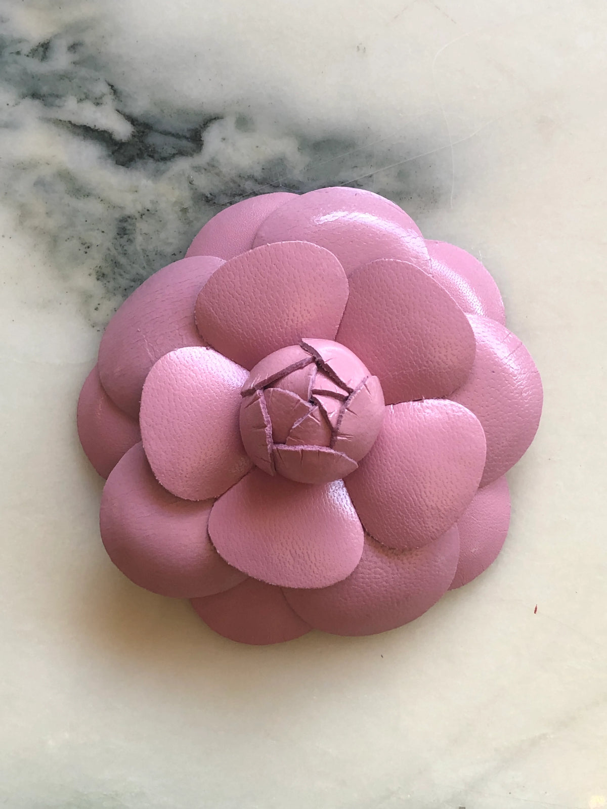 A Broochella Camelia handmade pink leather flower-shaped accessory brooch,  resting on a white marble surface.
