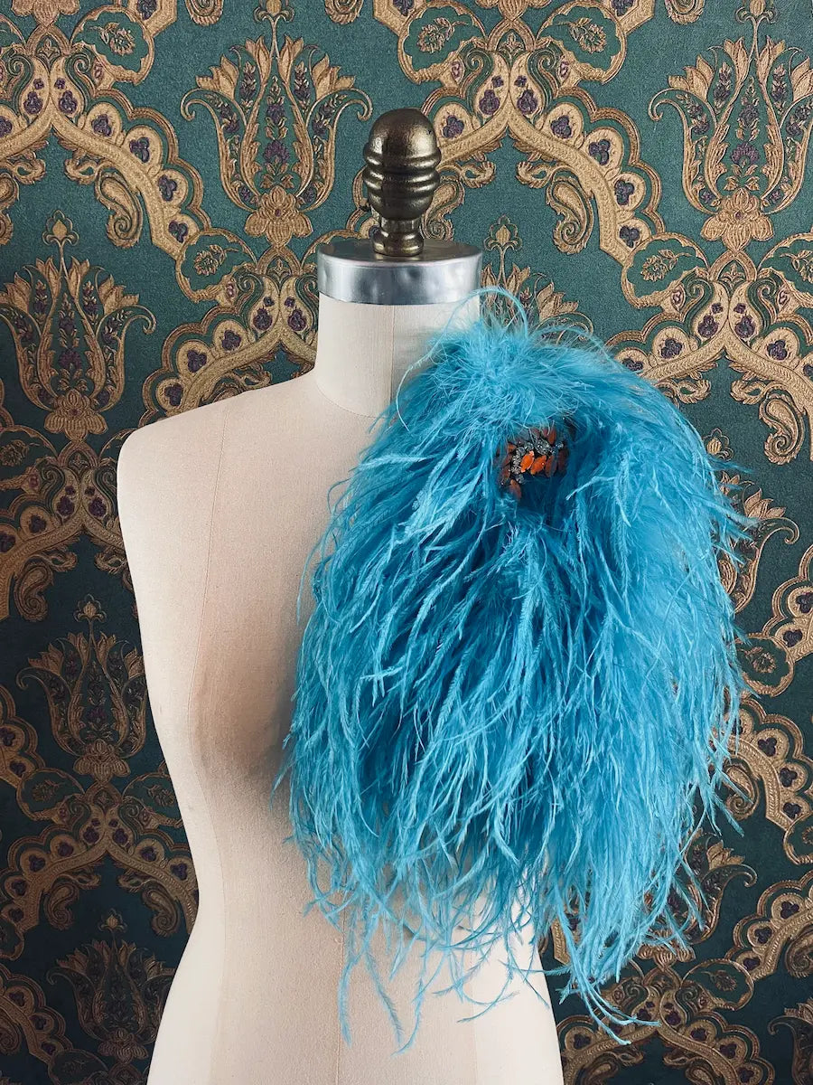 Broochella Piuma handmade neon blue feathered embellished designer brooch pictured on a mannequin the background is green and gold damask wallpaper