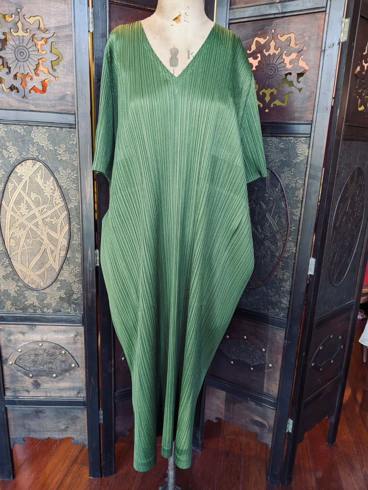 A Broochellaauthentic designer  Issey Miyake Pleated Please green pleated kaftan maxi dress displayed on a mannequin torso, set against a dark wooden folding screen.