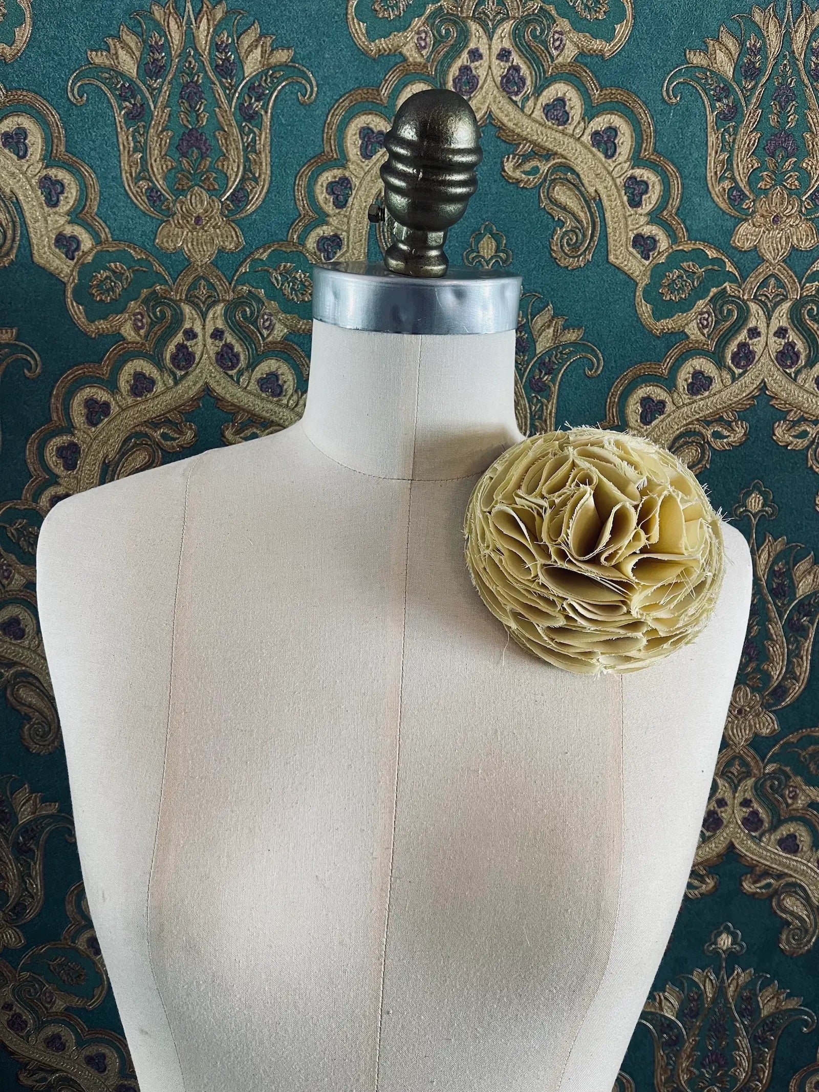 Broochella Pom Pon handmade designer flower brooch in yellow. Pictured on a mannequin. The background is green and gold damask wallpaper.