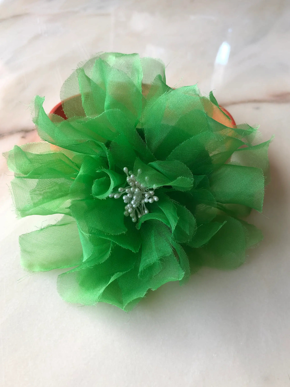 Broochella Poochella Aubrieta green pet flower featuring vibrant emerald-green sheer fabric petals and delicate white pearl-like stamens, attached to an orange dog collar, photographed on cream marble with natural grey veining.