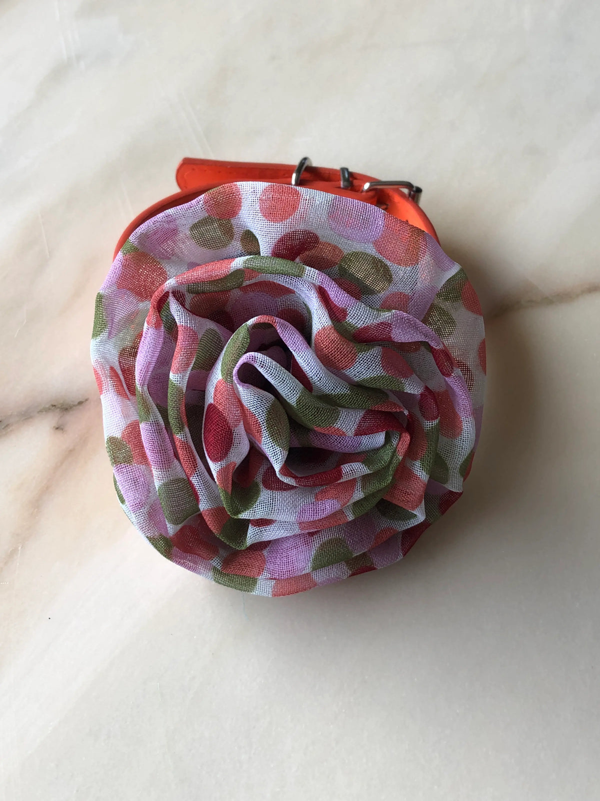 Broochella Poochella Brassica pink pet flower featuring sculptural layers of sheer white mesh fabric with pink, coral, lilac and olive-green polka dots, attached to an orange dog collar with silver hardware, photographed on cream marble with soft grey veining.