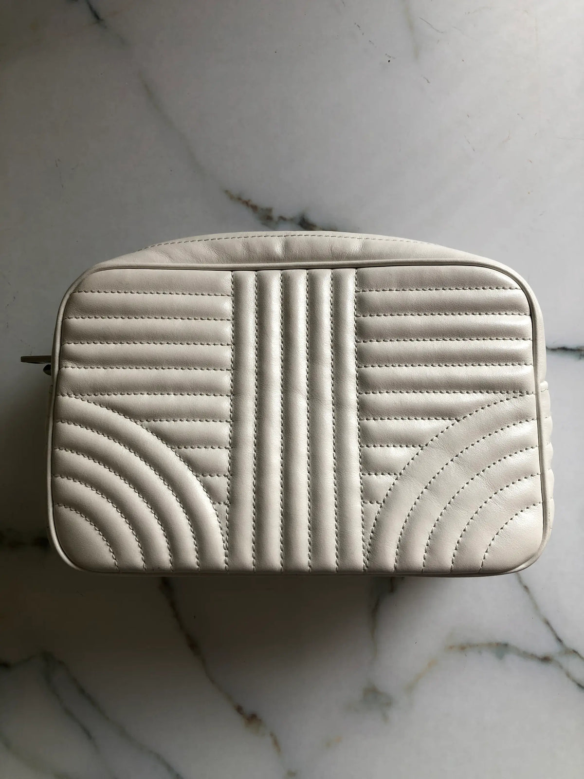 A cream-coloured quilted Broochella Prada bag with a geometric stitched pattern, shown from a top-down view on a white marble surface.