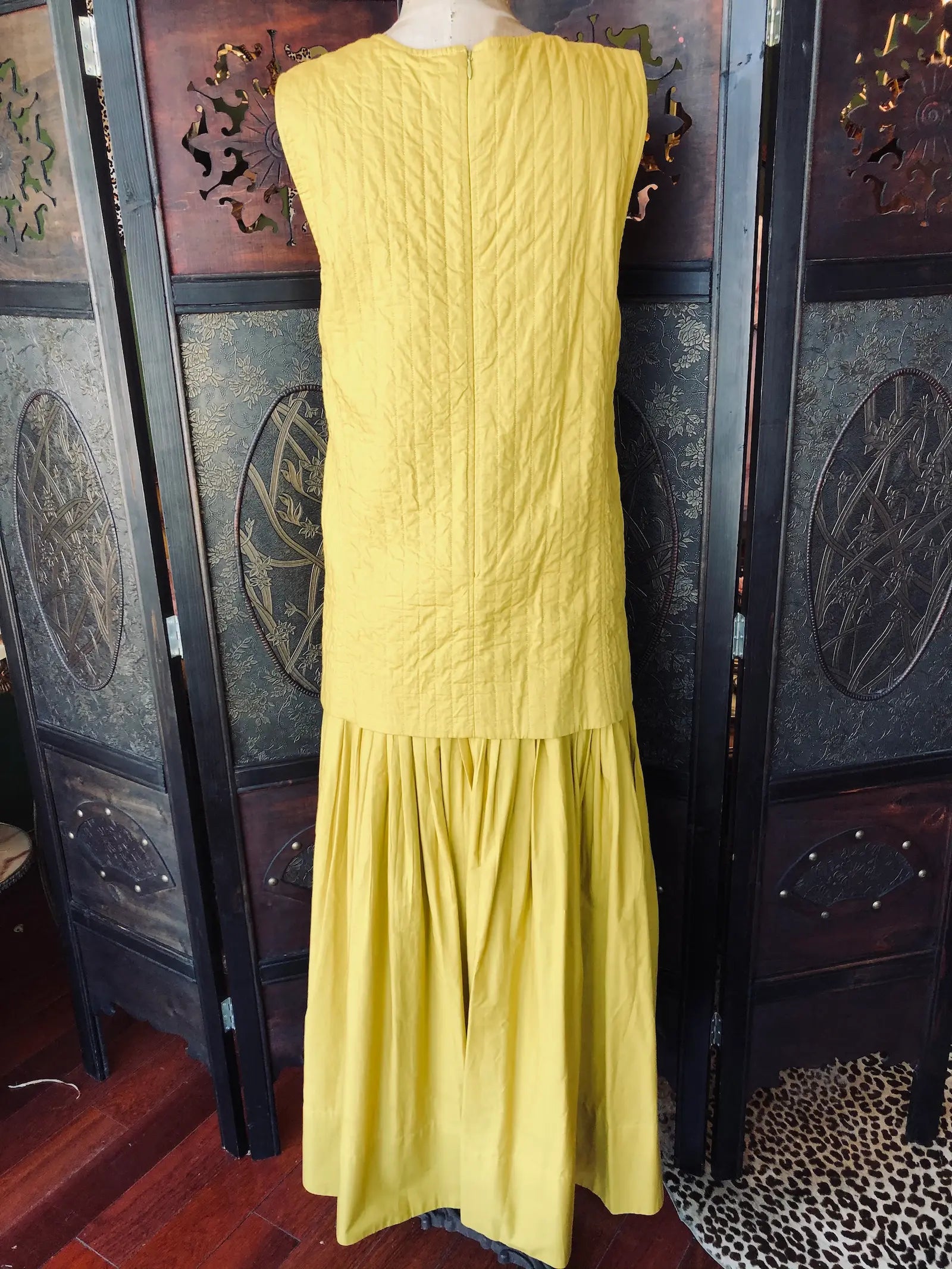 Broochella Rachel Comey XS maxi dress-back view. it is yellow and 100% Cotton. It is sleeveless with quilted, drop waist bodice and a scoop neck. It is pictured on a vintage mannequin. The background is an ornate, vintage, dark wood room divider. 