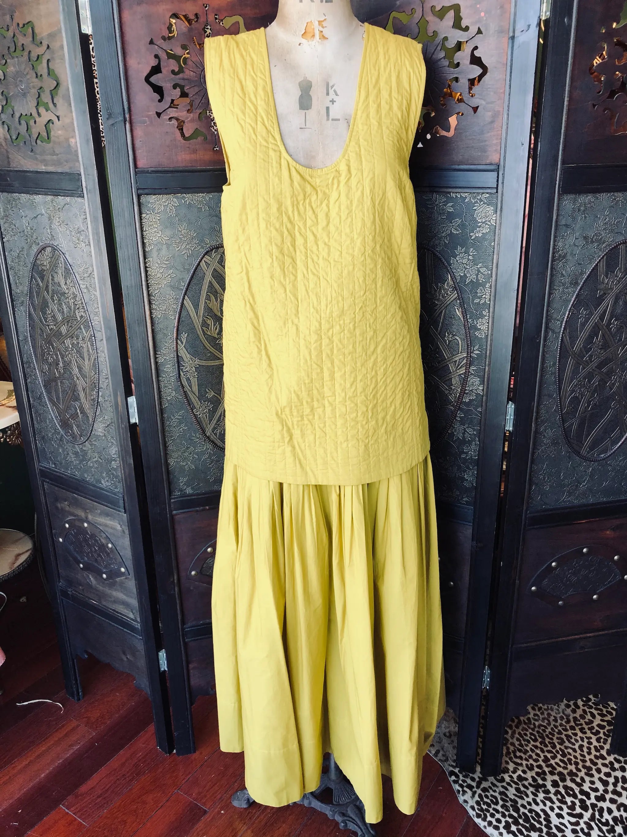 Broochella Rachel Comey XS maxi dress. it is yellow and 100% Cotton. It is 
Sleeveless with quilted, drop waist bodice and a scoop neck. It is pictured on a vintage mannequin. The background is an ornate, vintage, dark wood room divider. 