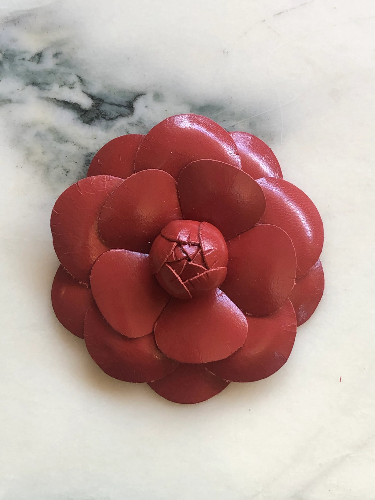 A Broochella Camelia handmade black leather flower-shaped accessory brooch,  resting on a white marble surface.