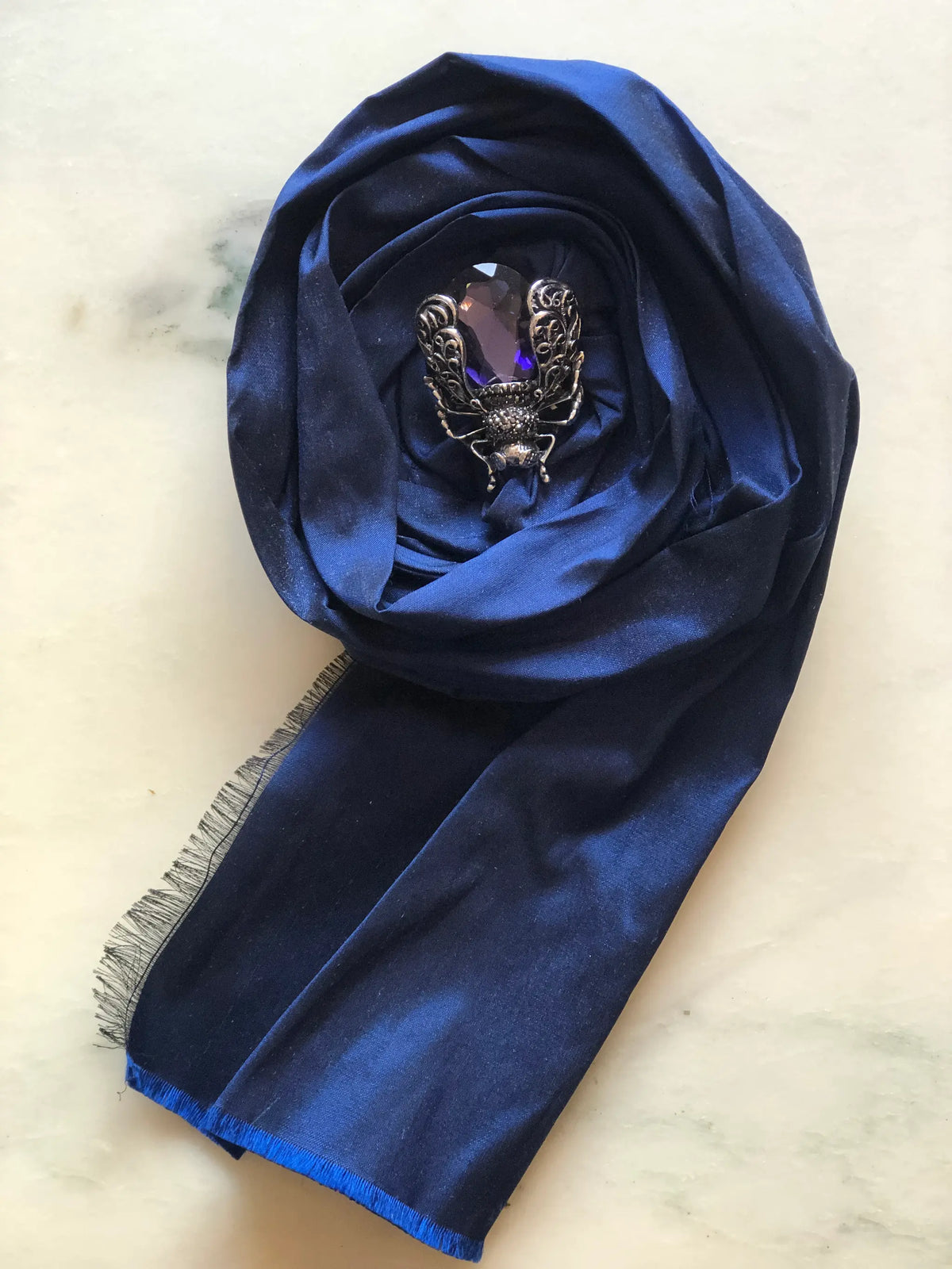 Broochella Rosa Ingioiellata Flower Brooch Pin - Small in rich navy blue silk, styled with a vintage blue crystal and silver-tone brooch at its centre on a cream marble background.