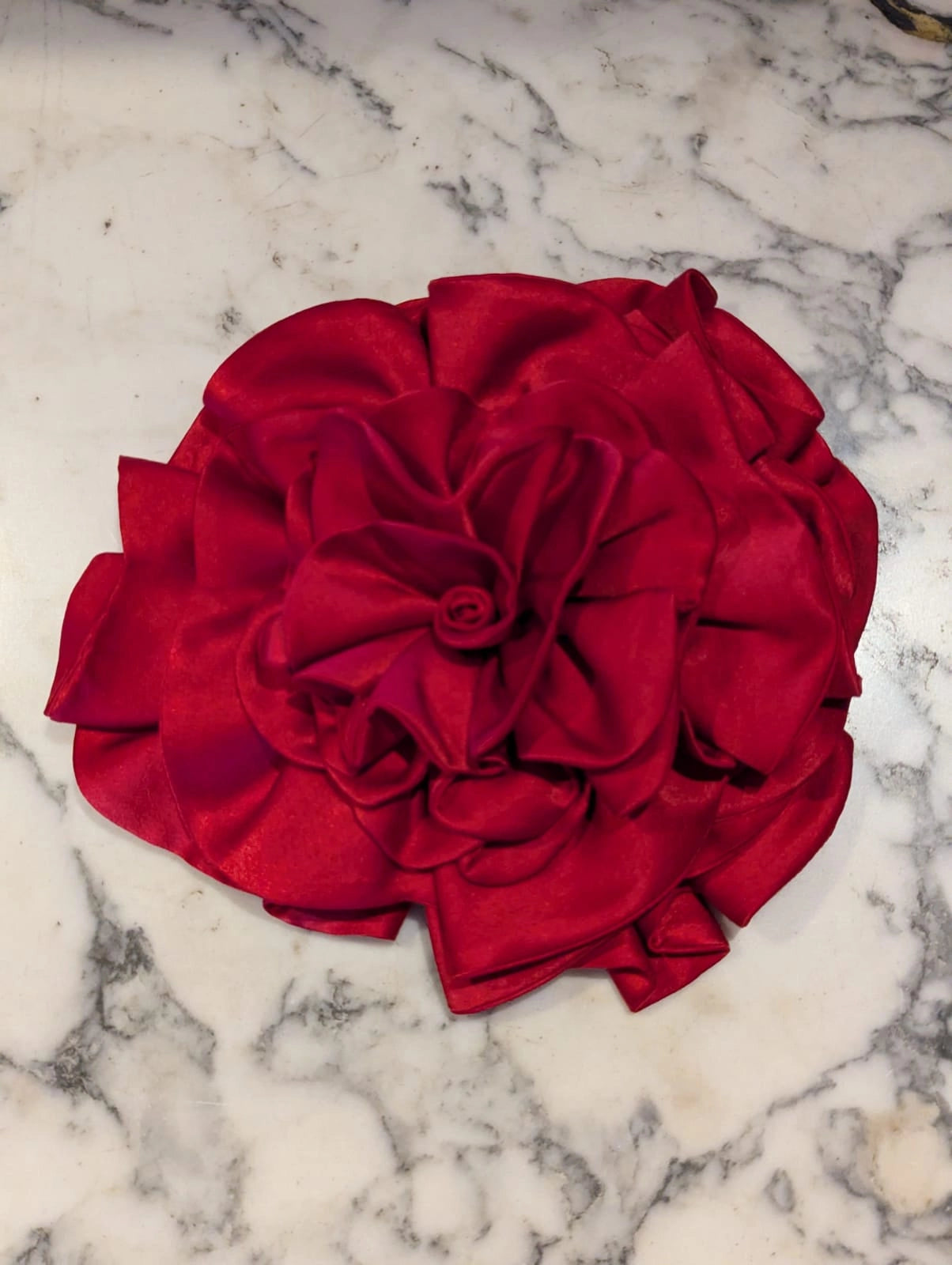 Broochella Rose de Minuit large, handmade, red satin flower brooch. It is pictured in a white marble surface.