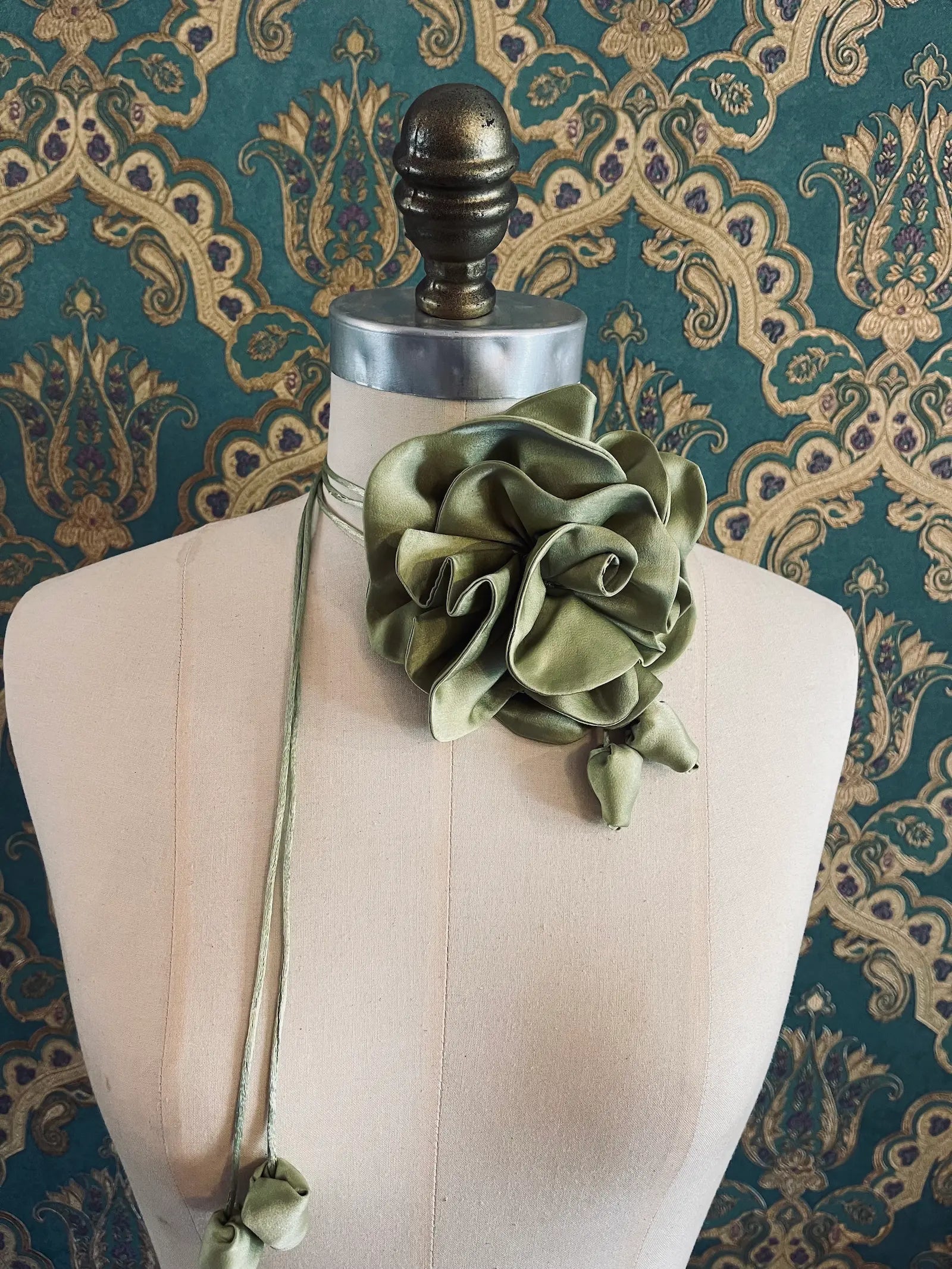 Broochella Rosetta avocado handmade silk satin flower brooch and choker  Pictured on a mannequin. The background is green and gold damask wallpaper