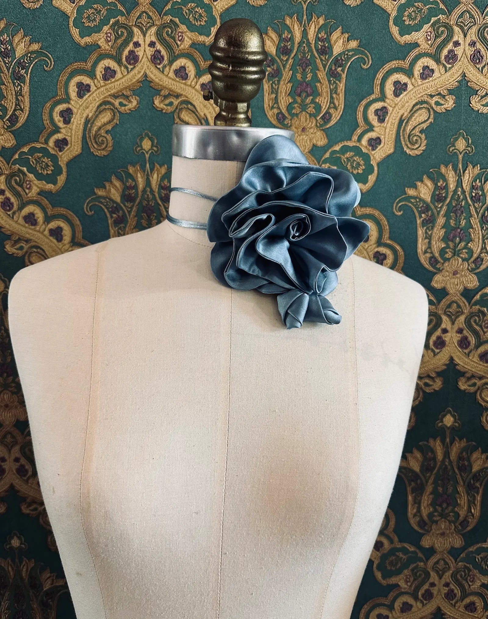 Broochella Rosetta blue handmade silk satin flower brooch and choker  Pictured on a mannequin. The background is green and gold damask wallpaper