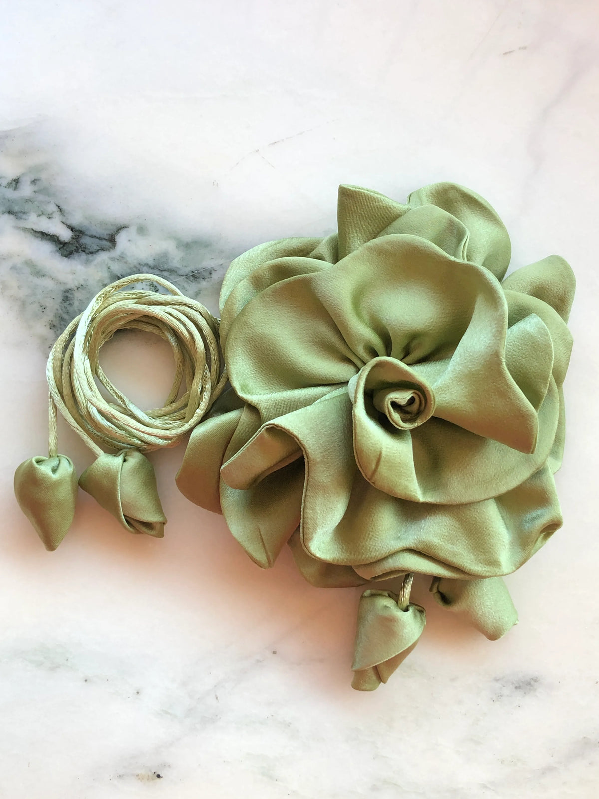 Broochella Rosetta avocado green flower choker and brooch with layered satin petals, matching tie cords and fabric buds, photographed on white marble with grey veining.