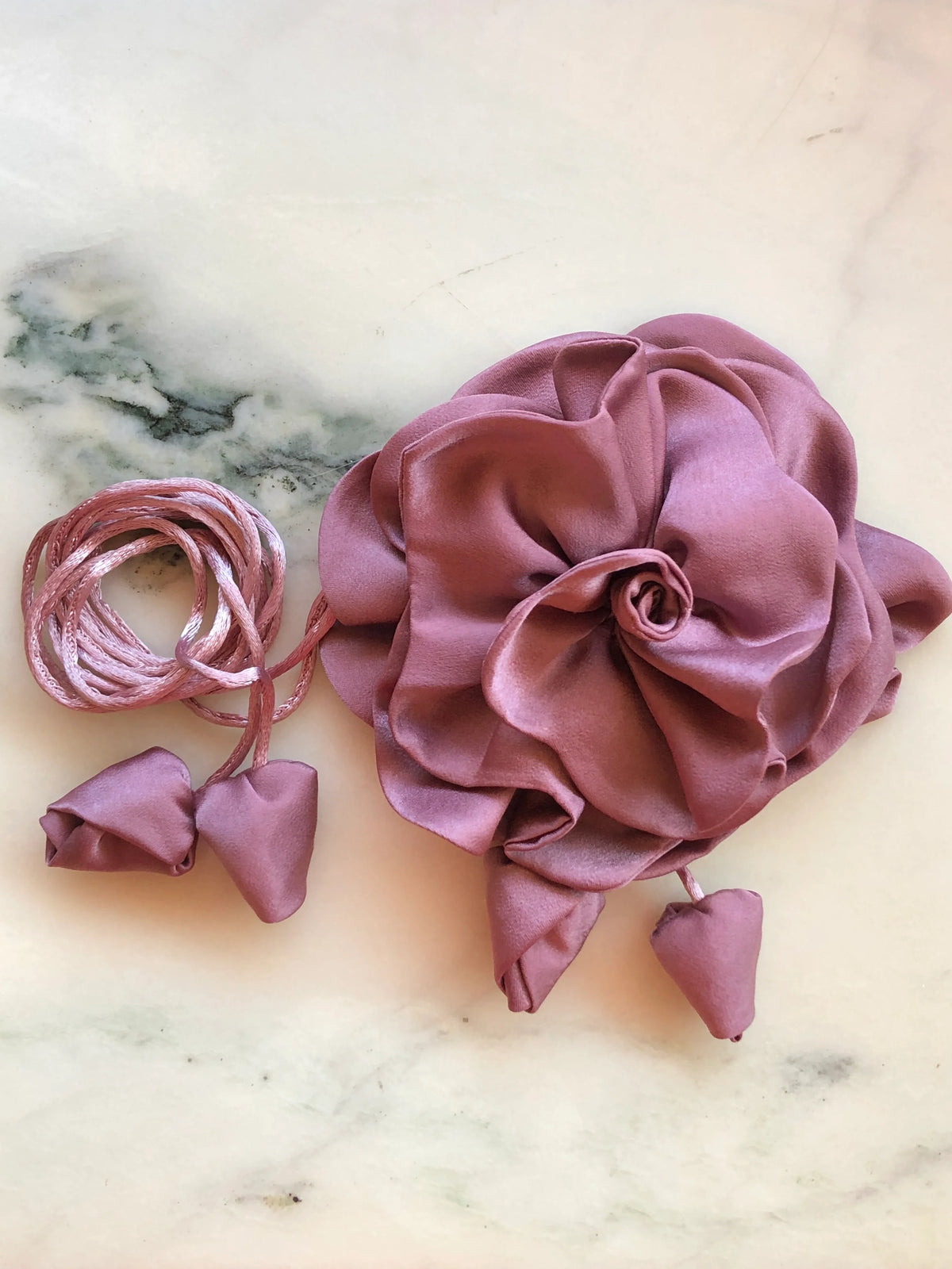 Broochella Rosetta blush pink flower choker and brooch with rich layered satin petals, matching tie cords and fabric buds, photographed on white marble with grey veining.