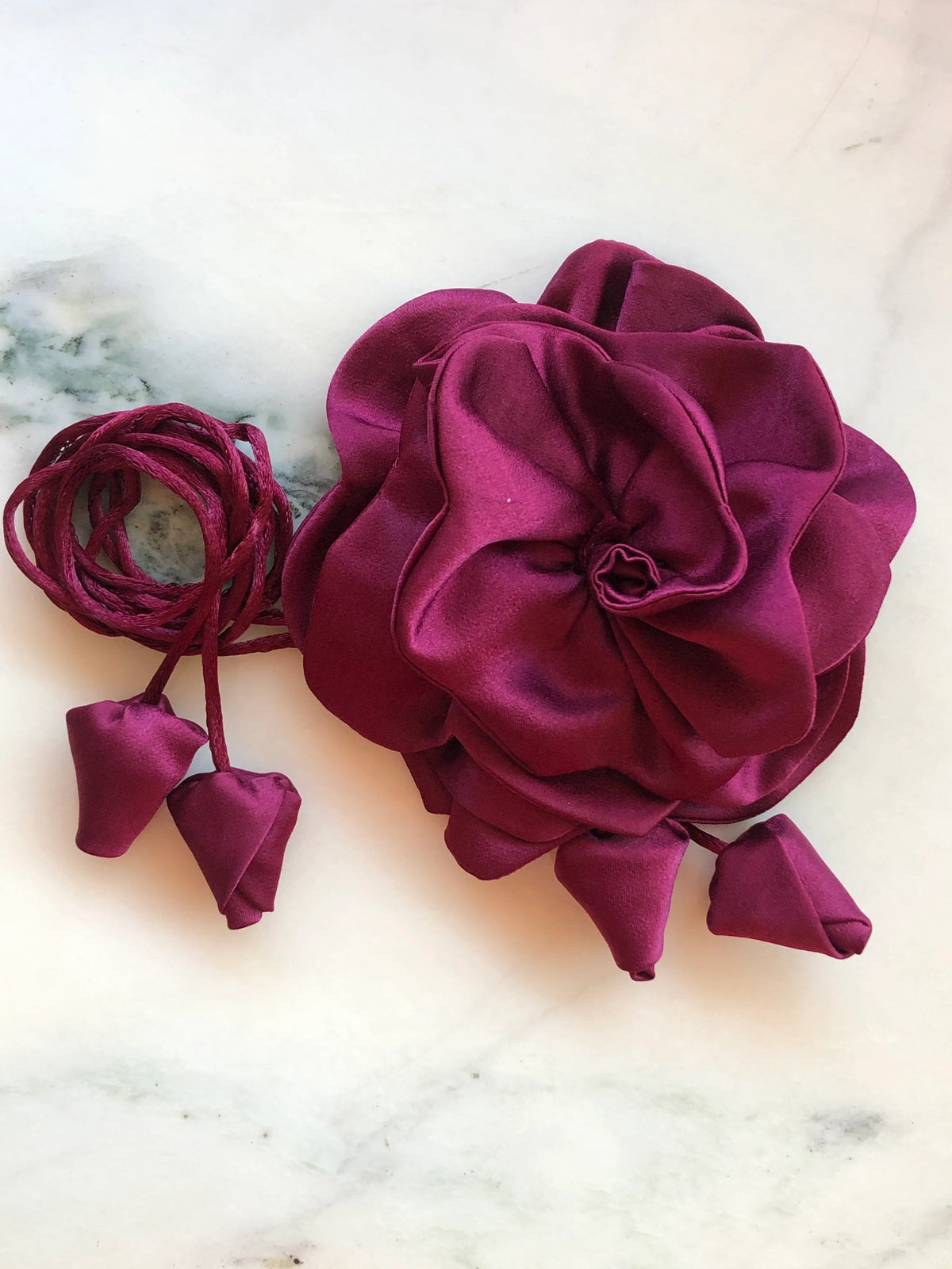 Broochella Rosetta burgundy flower choker and brooch with rich layered satin petals, matching tie cords and fabric buds, photographed on white marble with grey veining.