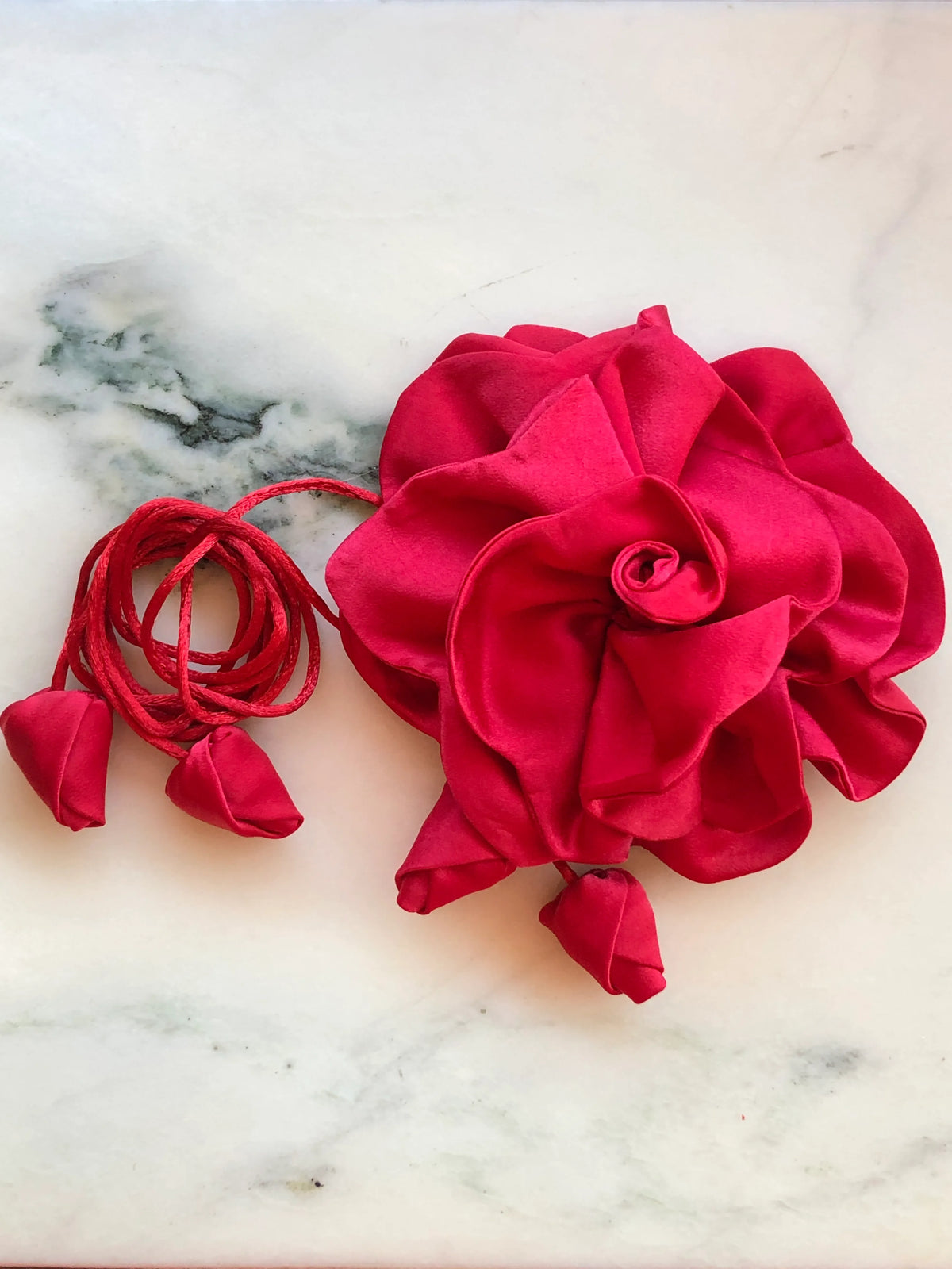 Broochella Rosetta red flower choker and brooch with layered satin petals, matching tie cords and fabric buds, photographed on white marble with grey veining.