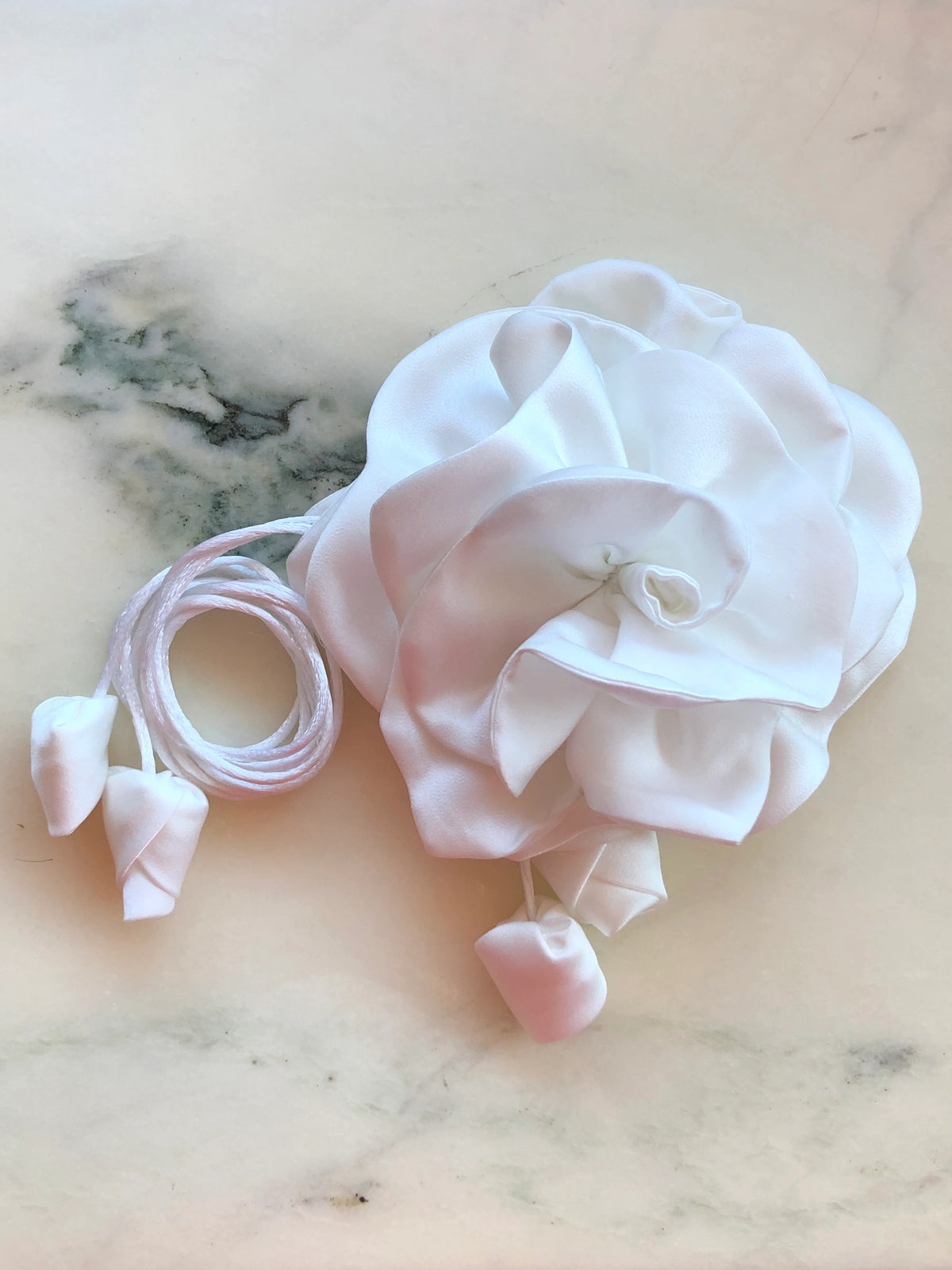 Broochella Rosetta white flower choker and brooch with sculptural satin petals, matching tie cords and fabric buds, photographed on white marble with grey veining.