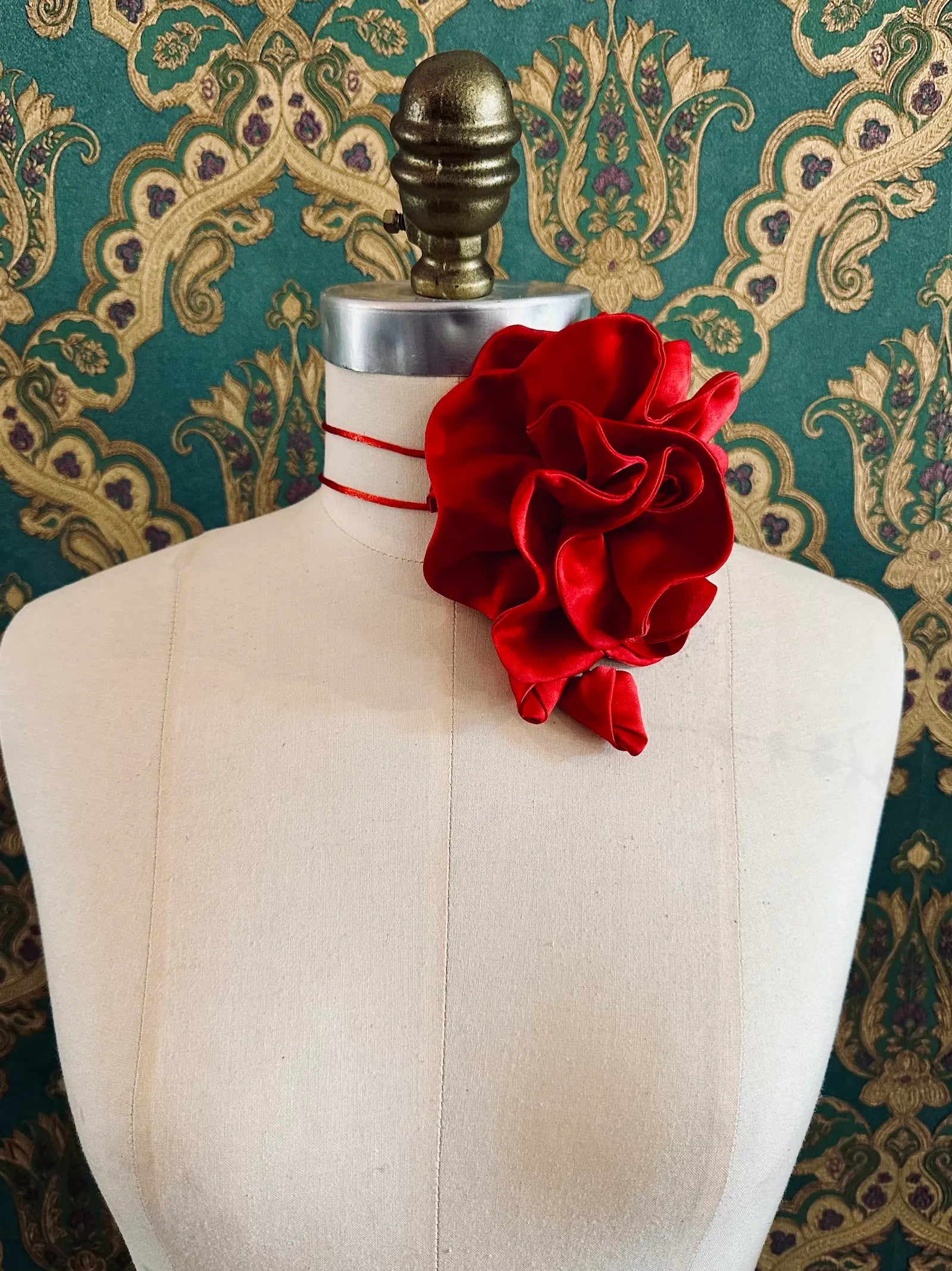 Broochella Rosetta red handmade silk satin flower brooch and choker  Pictured on a mannequin. The background is green and gold damask wallpaper