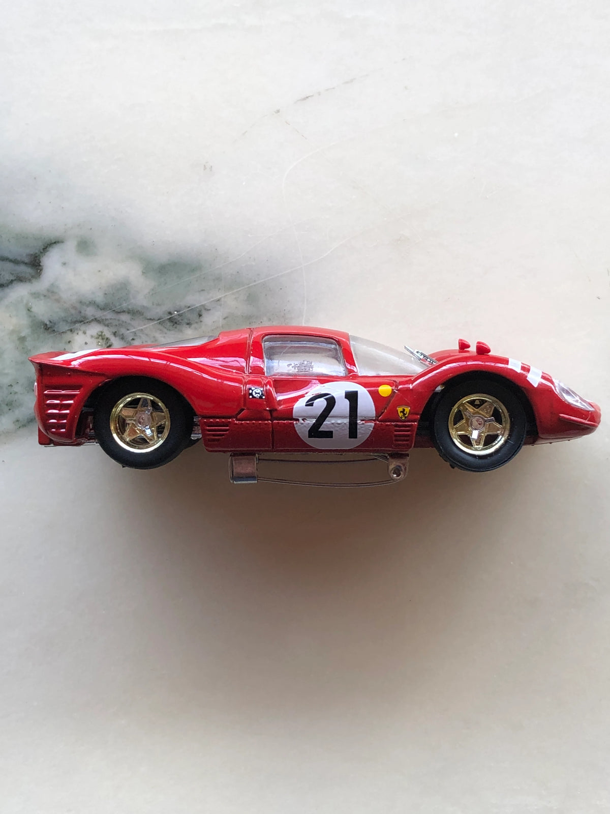 Broochella Rosso Fiorentino No.21 Vintage Endurance Racing Car Brooch for men in side profile, featuring a streamlined red body, white number 21 racing roundel, gold five-spoke wheels, Ferrari-style racing emblem and metal brooch pin fastening underneath.