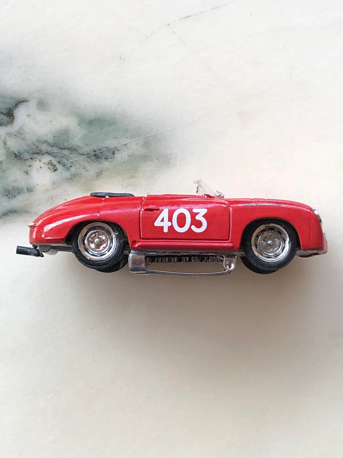 Broochella Rosso Mille No.403 Vintage Convertible Racing Car Brooch in side profile, featuring a streamlined red body, bold white number 403 racing decal, silver wheels, open-top design and metal brooch pin fastening underneath.