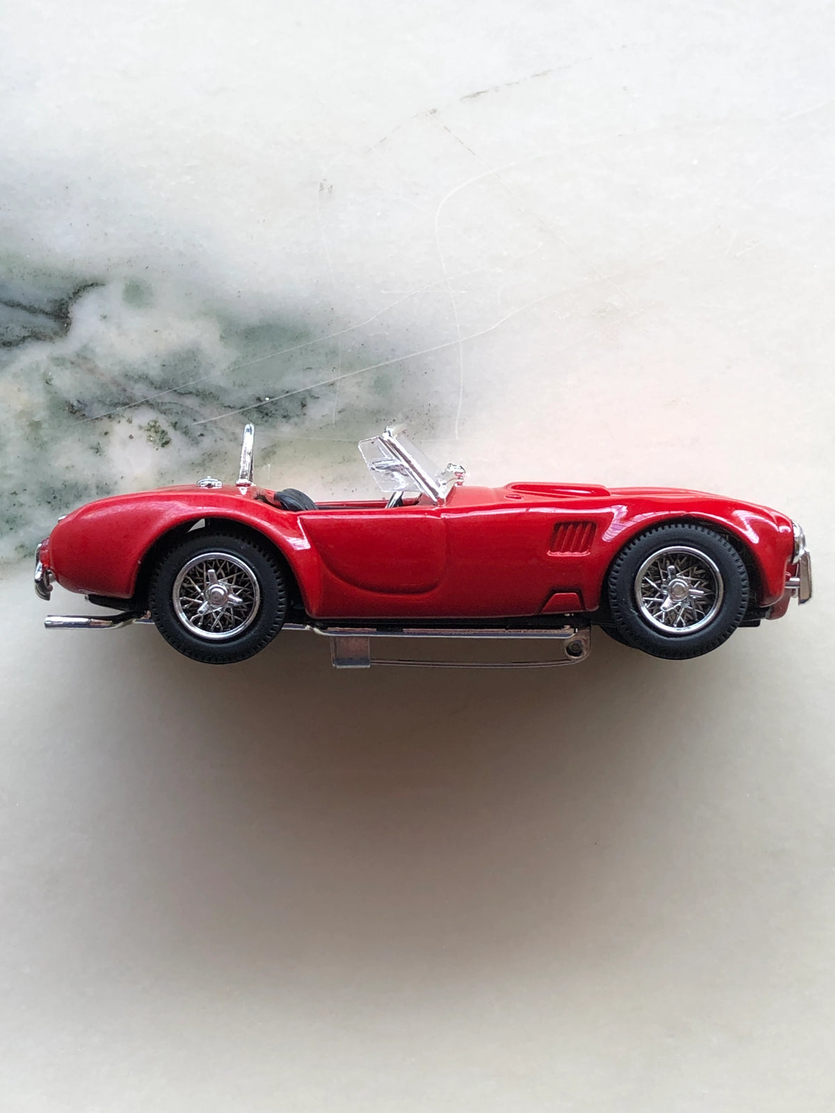 Broochella Rosso Roadster No.427 Vintage Convertible Racing Car Brooch in side profile, featuring a glossy red open-top sports car silhouette, black interior, chrome windscreen, silver wire-spoke wheels and metal brooch pin fastening underneath.