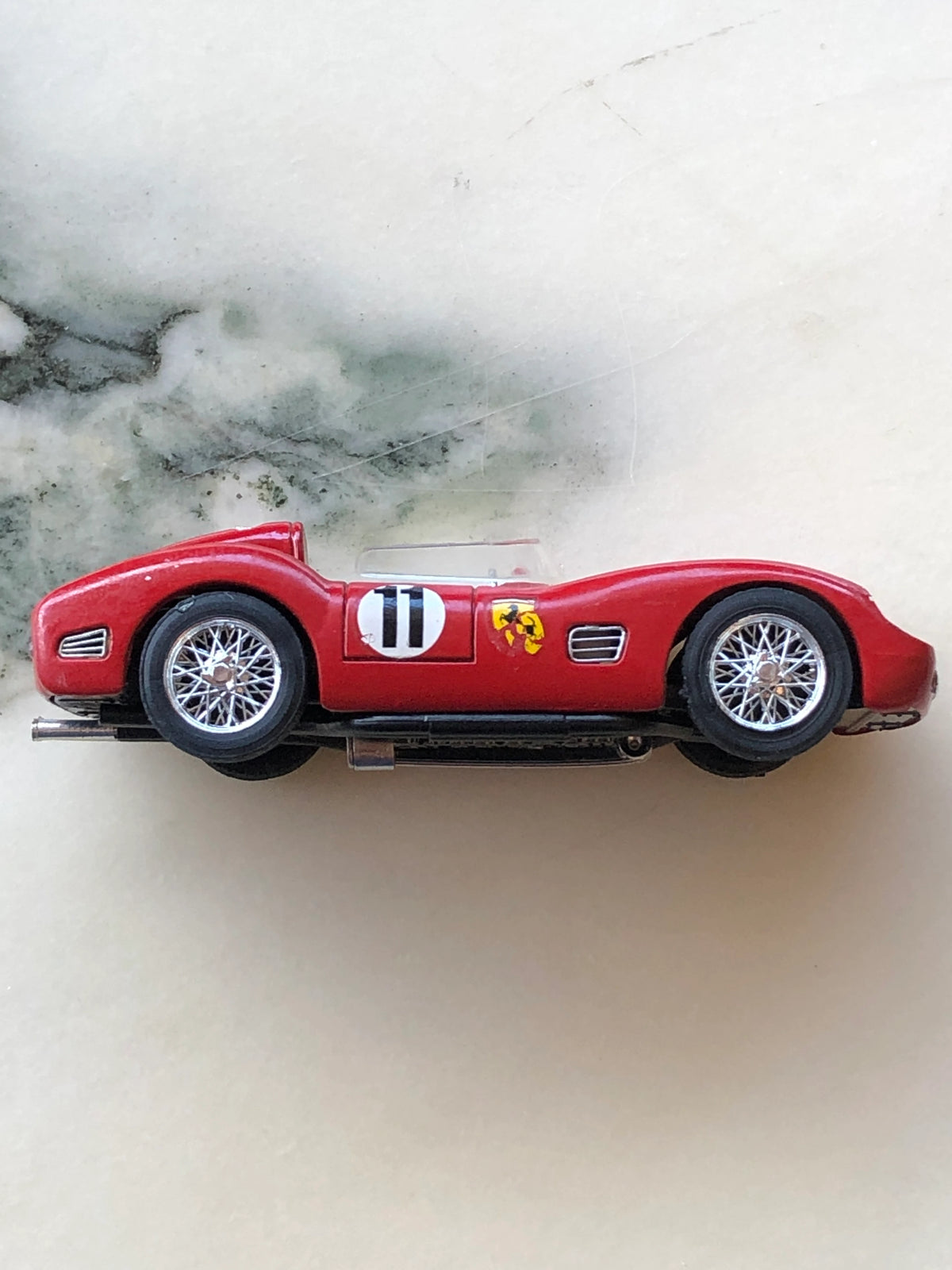 Broochella Rosso Sprint No.11 Vintage Open-Top Racing Car Brooch in side profile, showcasing its streamlined red body, black number 11 racing decal, yellow prancing horse emblem, silver wire-spoke wheels and brooch pin fastening beneath.