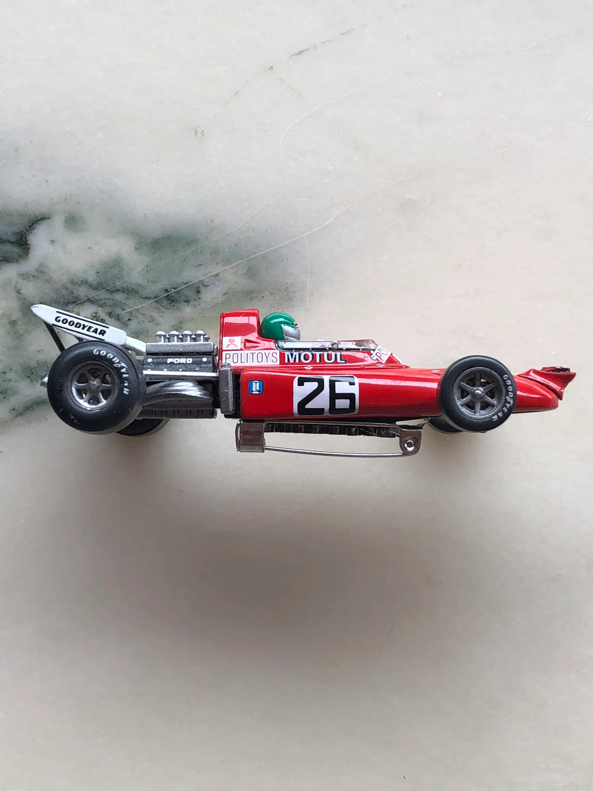 Broochella Rosso Turbo No.26 Vintage Formula Racing Car Brooch in side profile, featuring a red Formula racing car with number 26, Goodyear tyres, silver Ford engine, green driver's helmet and vintage Motul sponsorship decals.