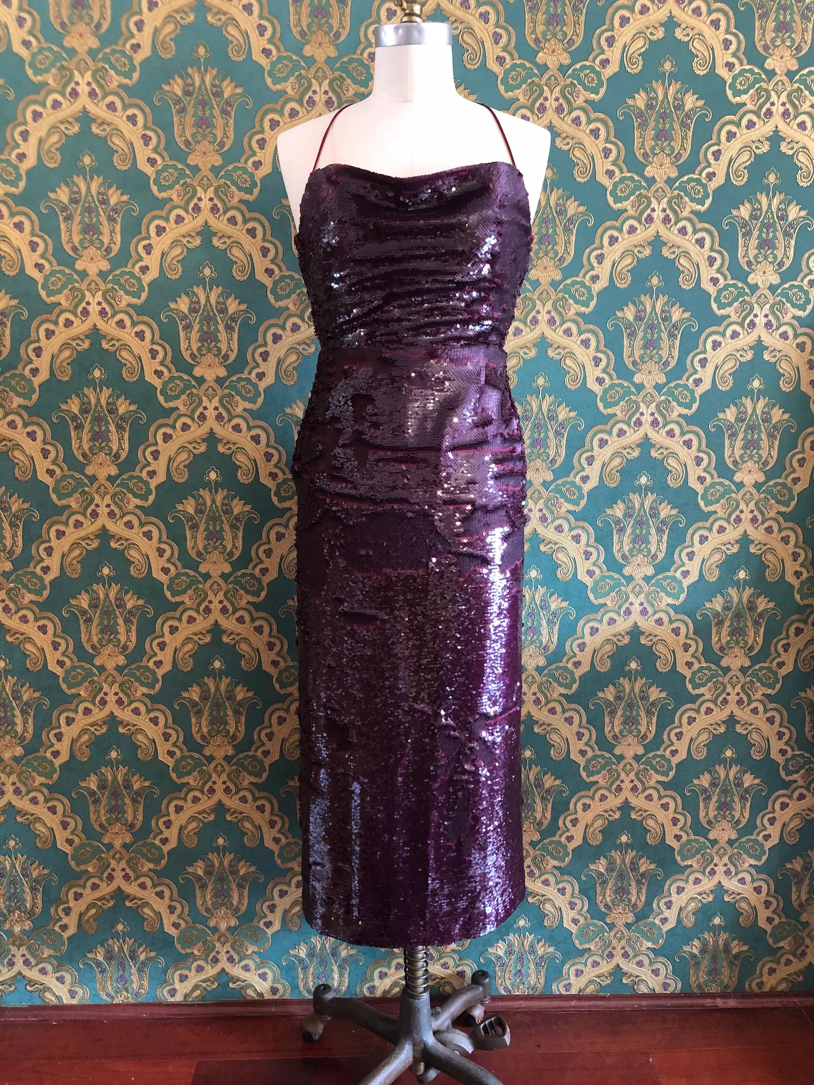 Broochella Sabina Musáyev Zarya midi dress in Ruby Wine with tonal sequins, cowl neckline and lace-up back, size XS. Pictures on a mannequin. The background is green and gold damask wallpaper