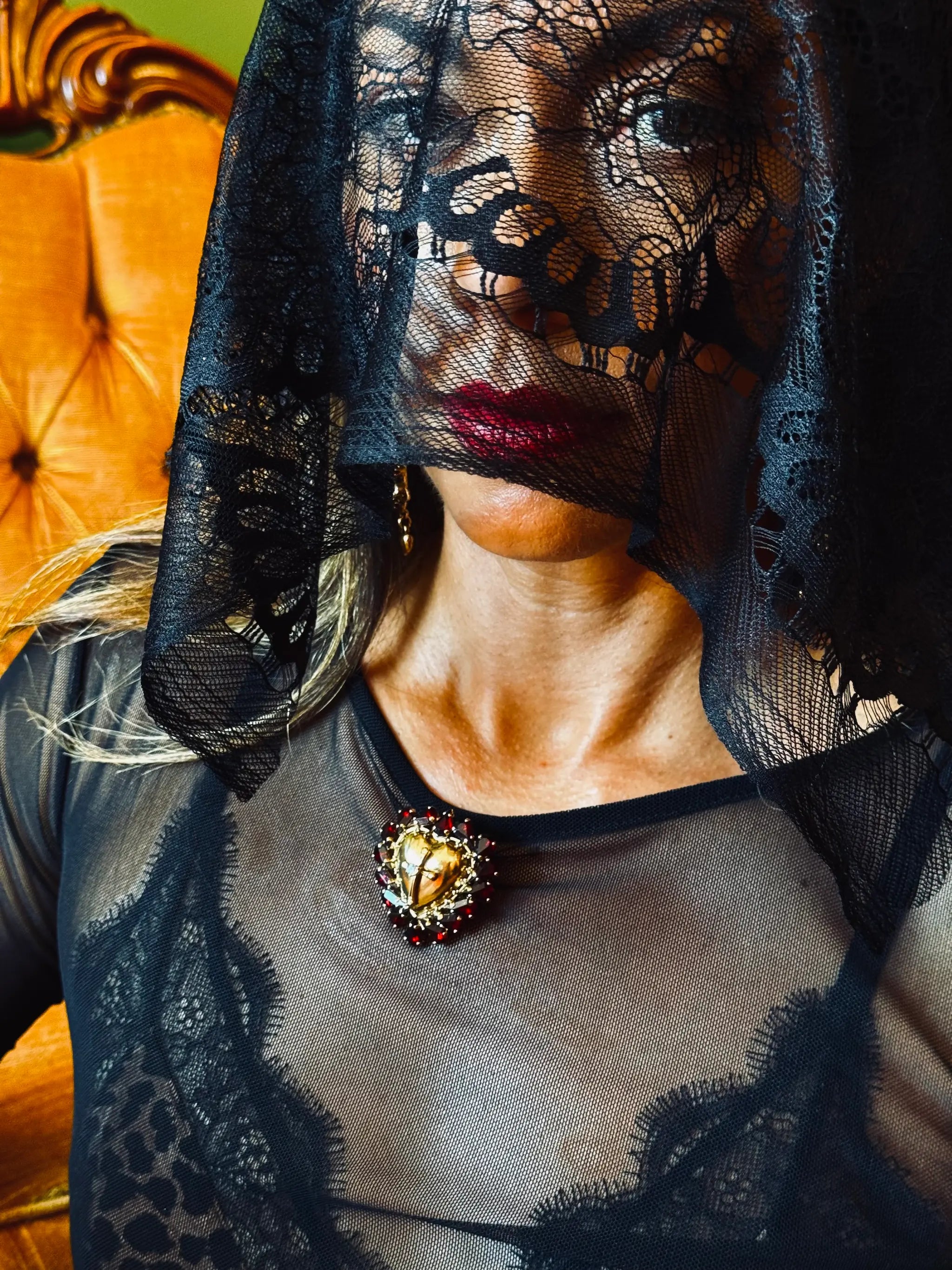 Broochella sacro cuore cristo heart and crucifix brooch with red crystal frame. It is pinned to the sheer black dress of a model. She is wearing a black lace veil