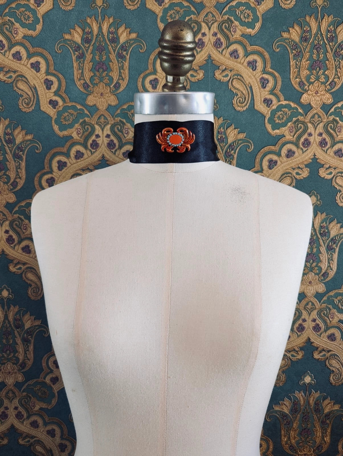 Broochella Sacro cuore granchio orange crab shaped brooch. Pinned to a mannequin. The background is green and gold damask wallpaper