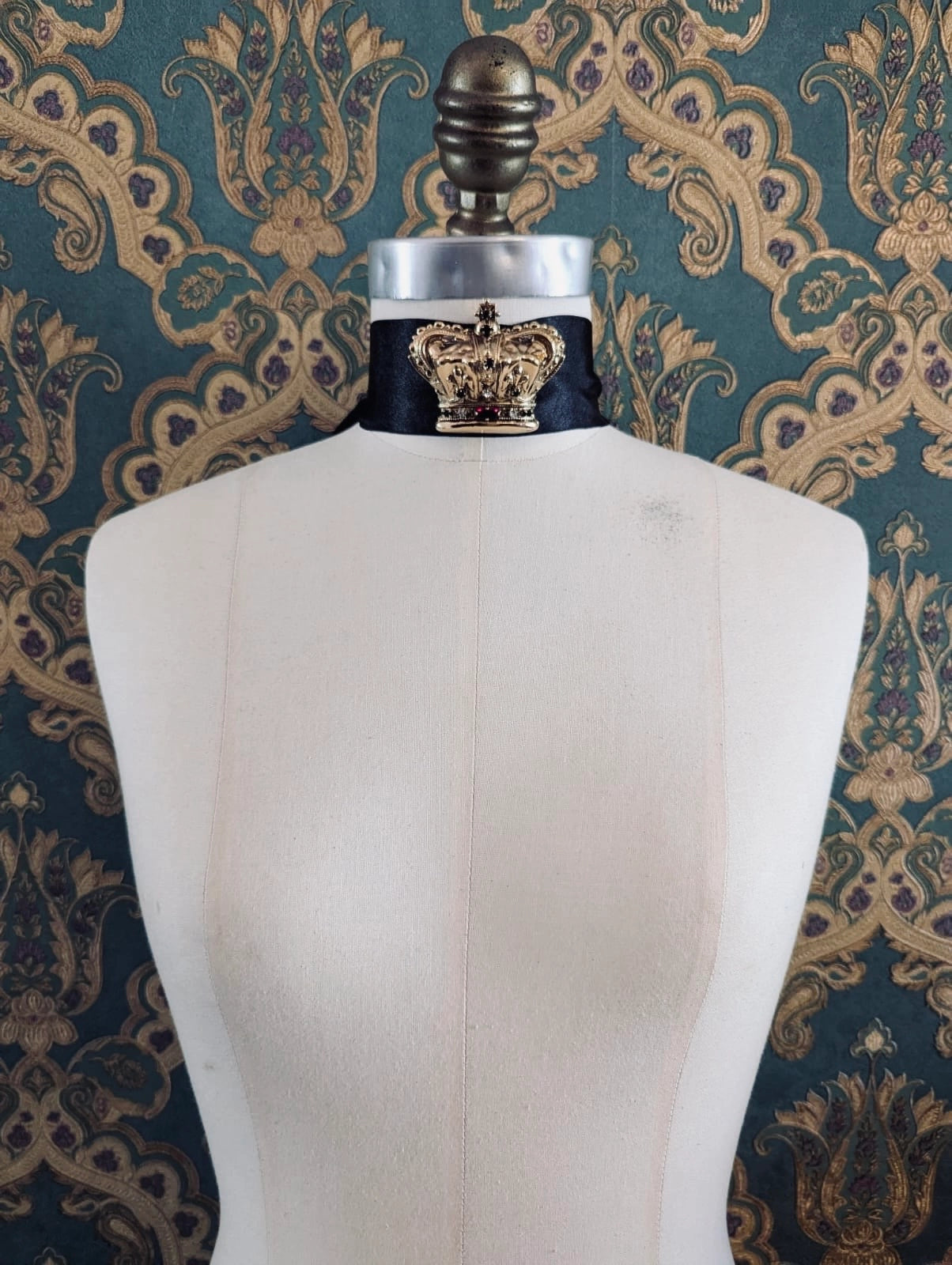 Broochella Sacro cuore regina gold designer crown brooch. Pinned to a mannequin. The background is green and gold damask wallpaper