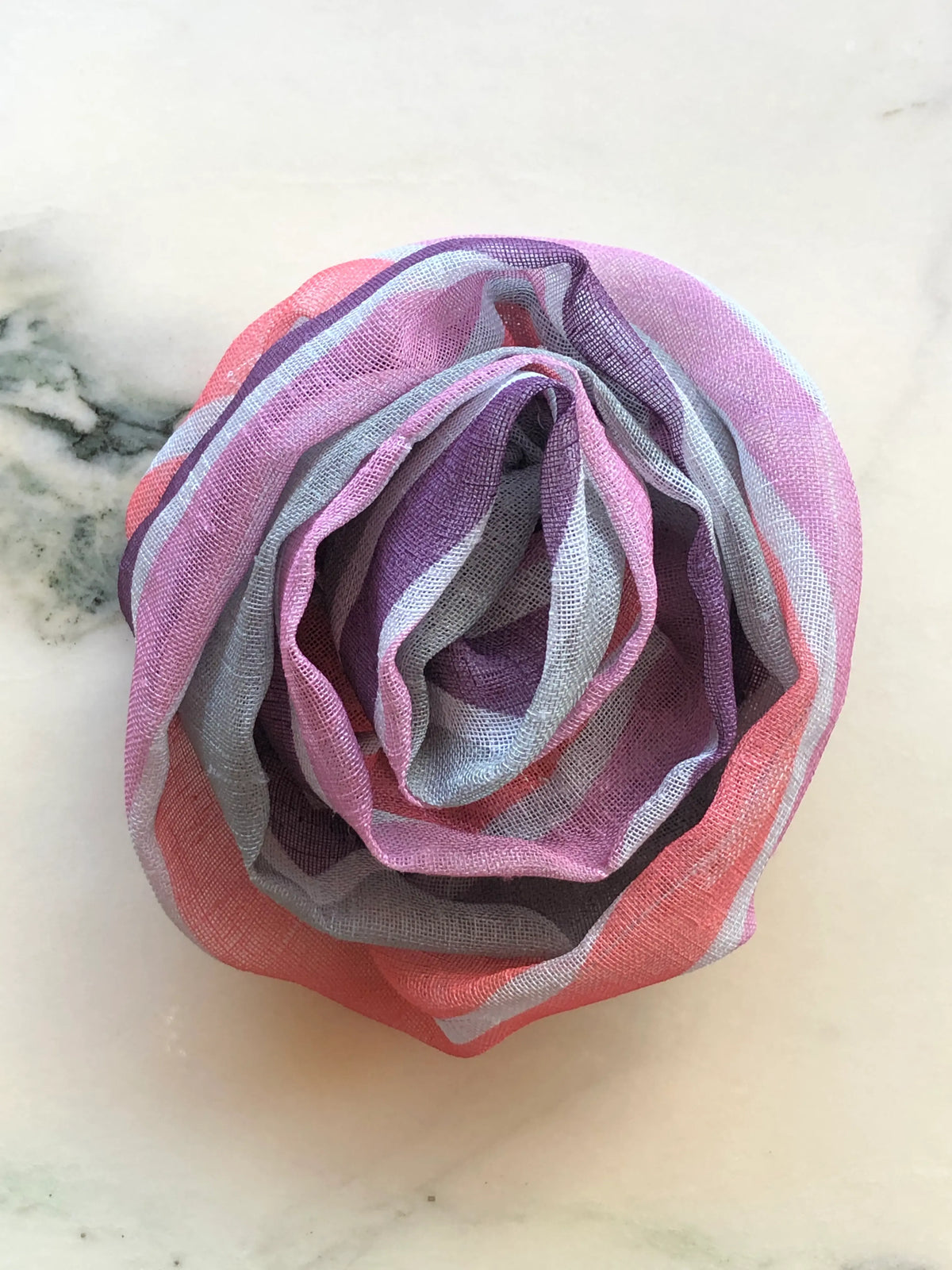 Broochella Serena Fiore Striped Linen Bloom Brooch featuring sculptural layered linen petals in pink, lilac, coral, grey and white stripes on a white marble background.
