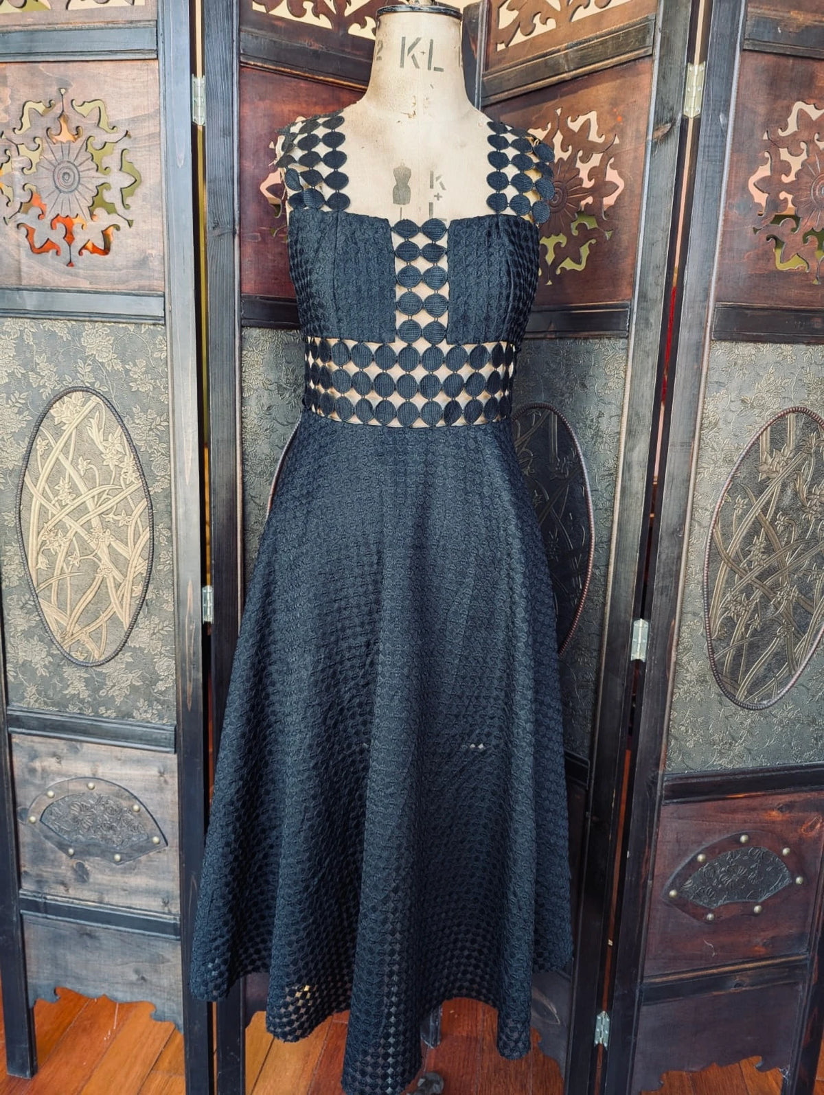 Broochella Shakuhachi Black Cut-Out Midi Dress – Size S. Pictured on a mannequin. The background is an ornate dark wood room divider. 