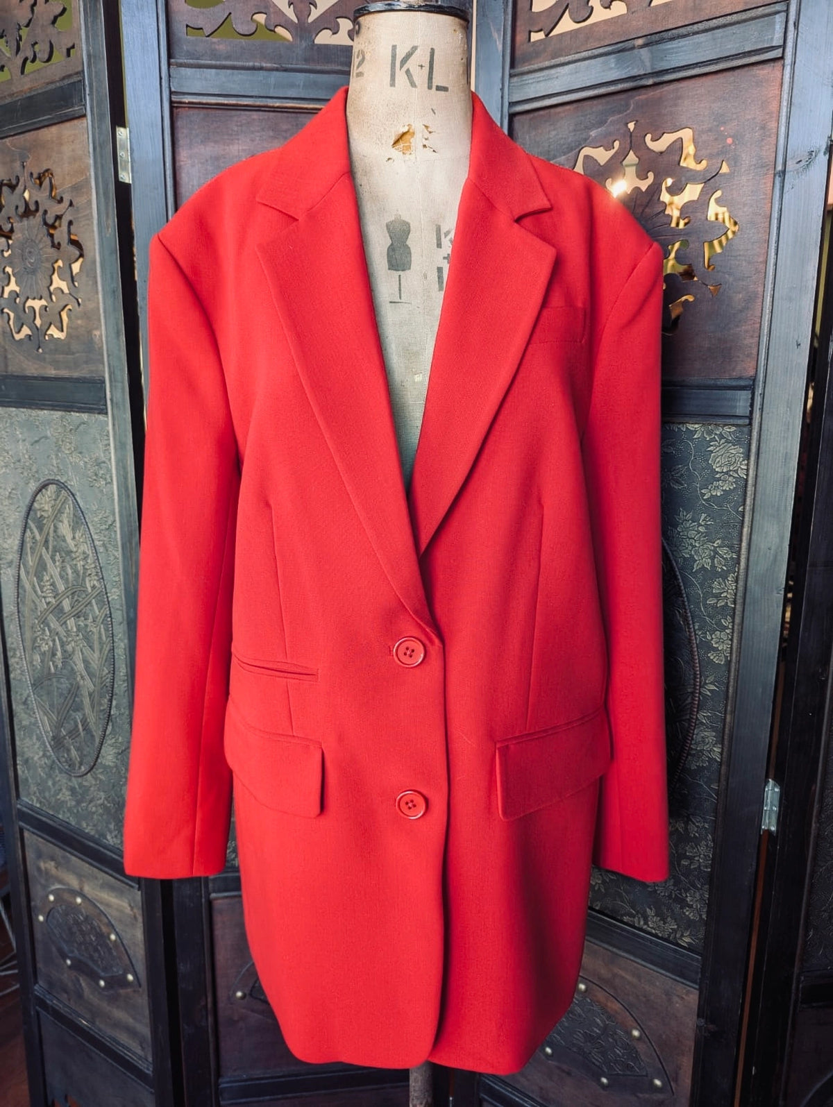 Broochella Shona Joy red longline blazer. It is pictured on a mannequin. The background is an ornate dark wood room divider. 