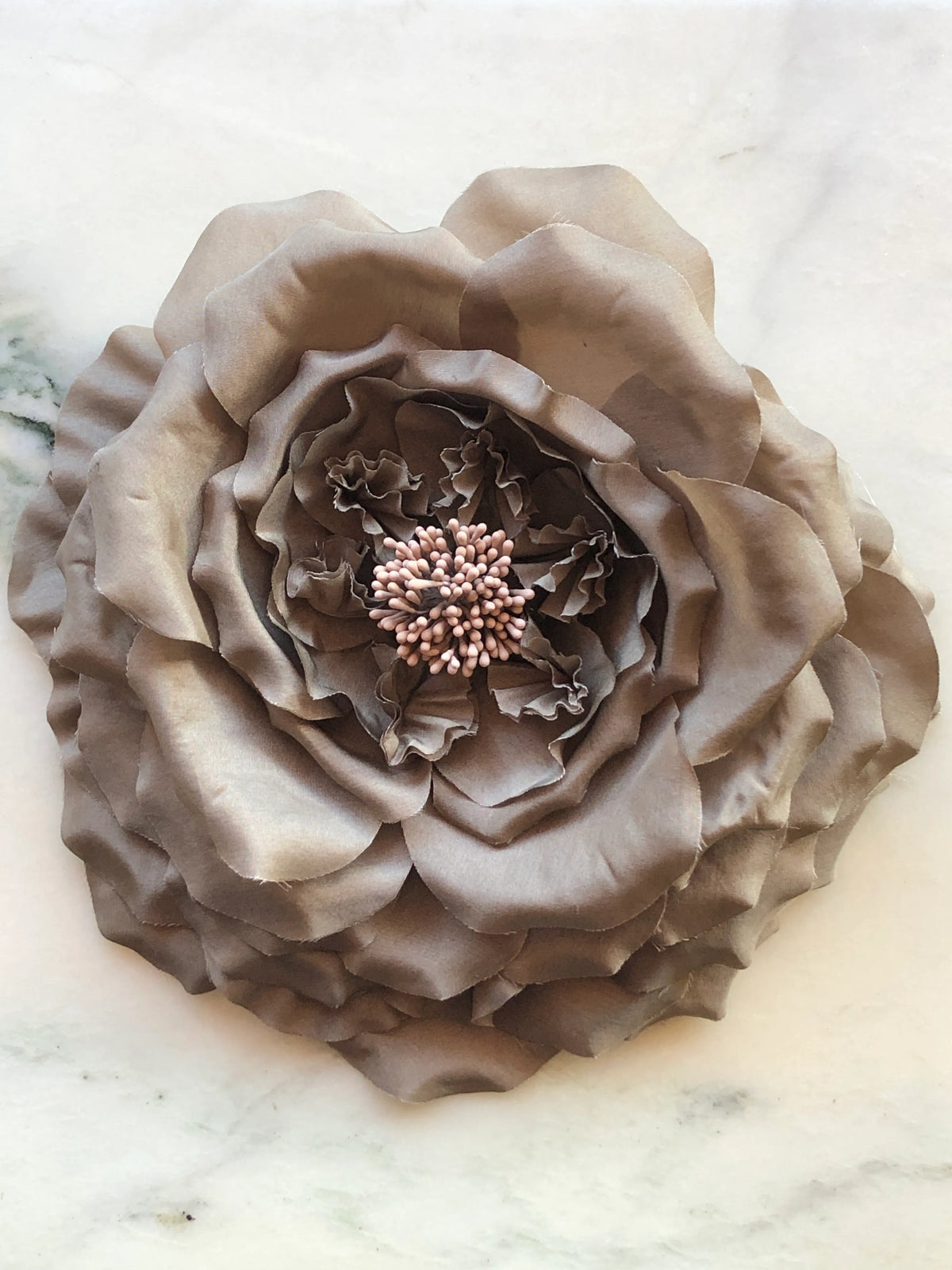 Broochella Signora Fiorita Flower Brooch Pin in soft brown with layered fabric petals and a textured stamen centre, photographed on a white marble background with grey veining.